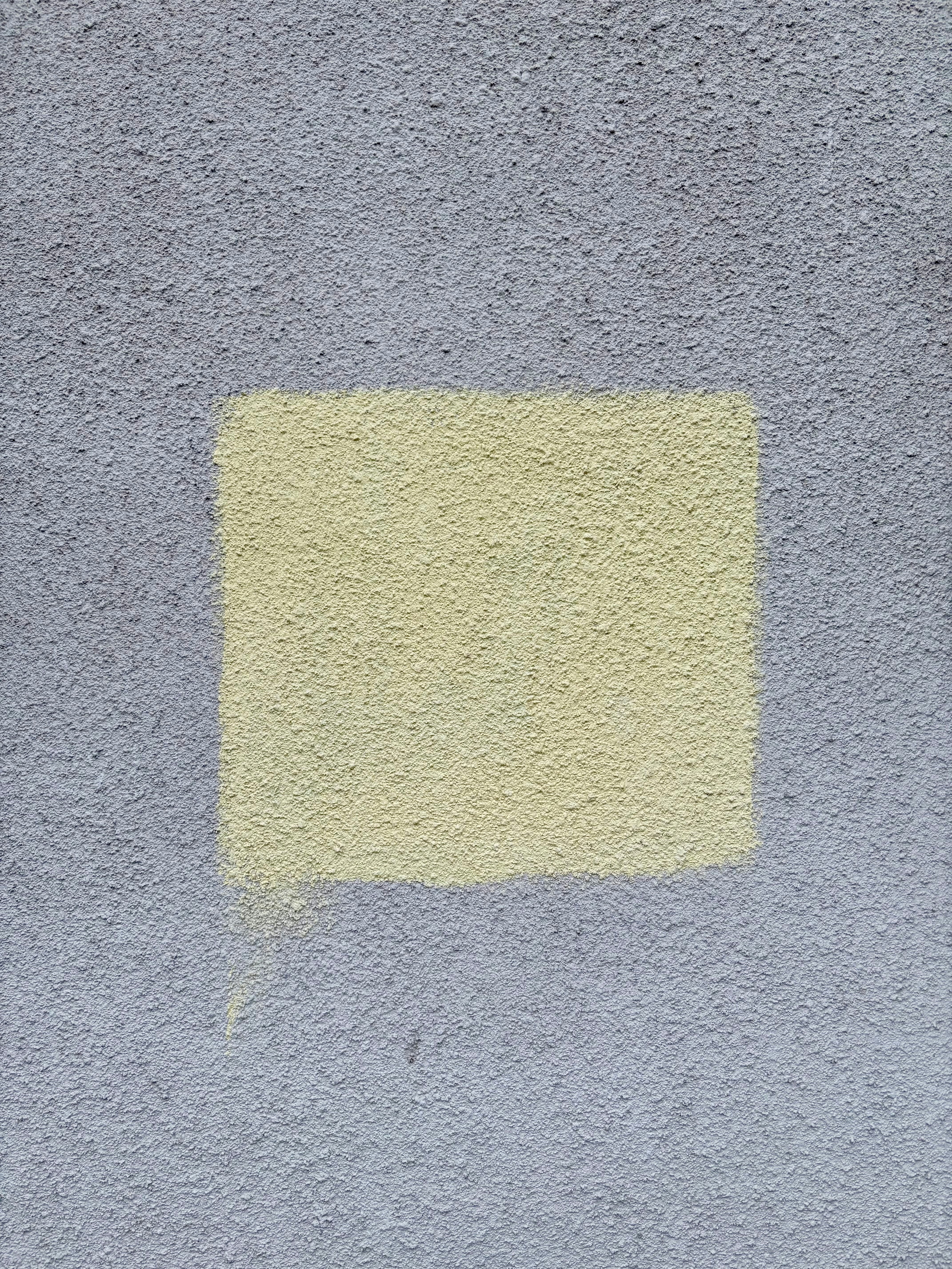 A yellow square is painted on a gray wall.