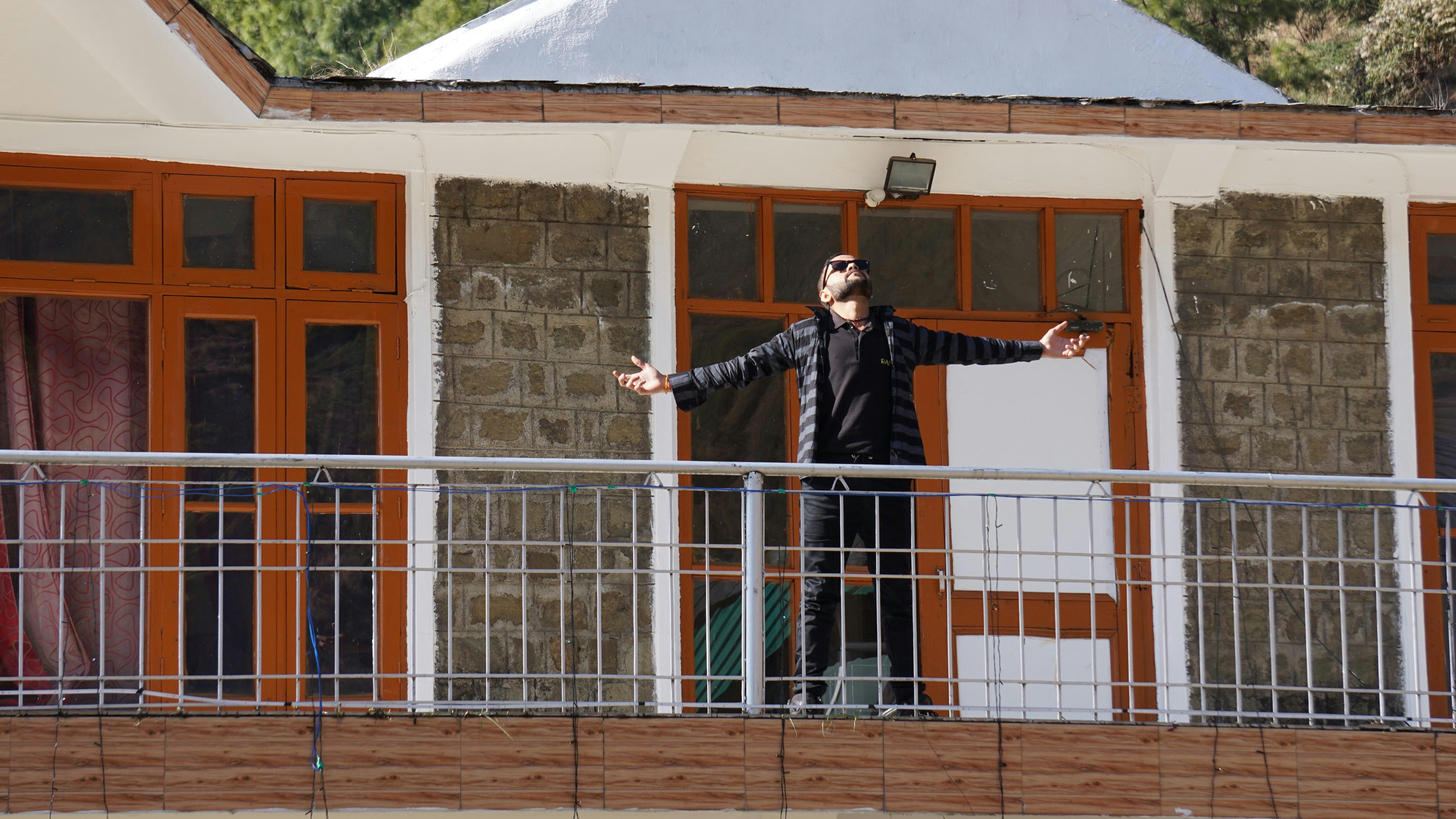 Man stands on a balcony with arms outstretched.