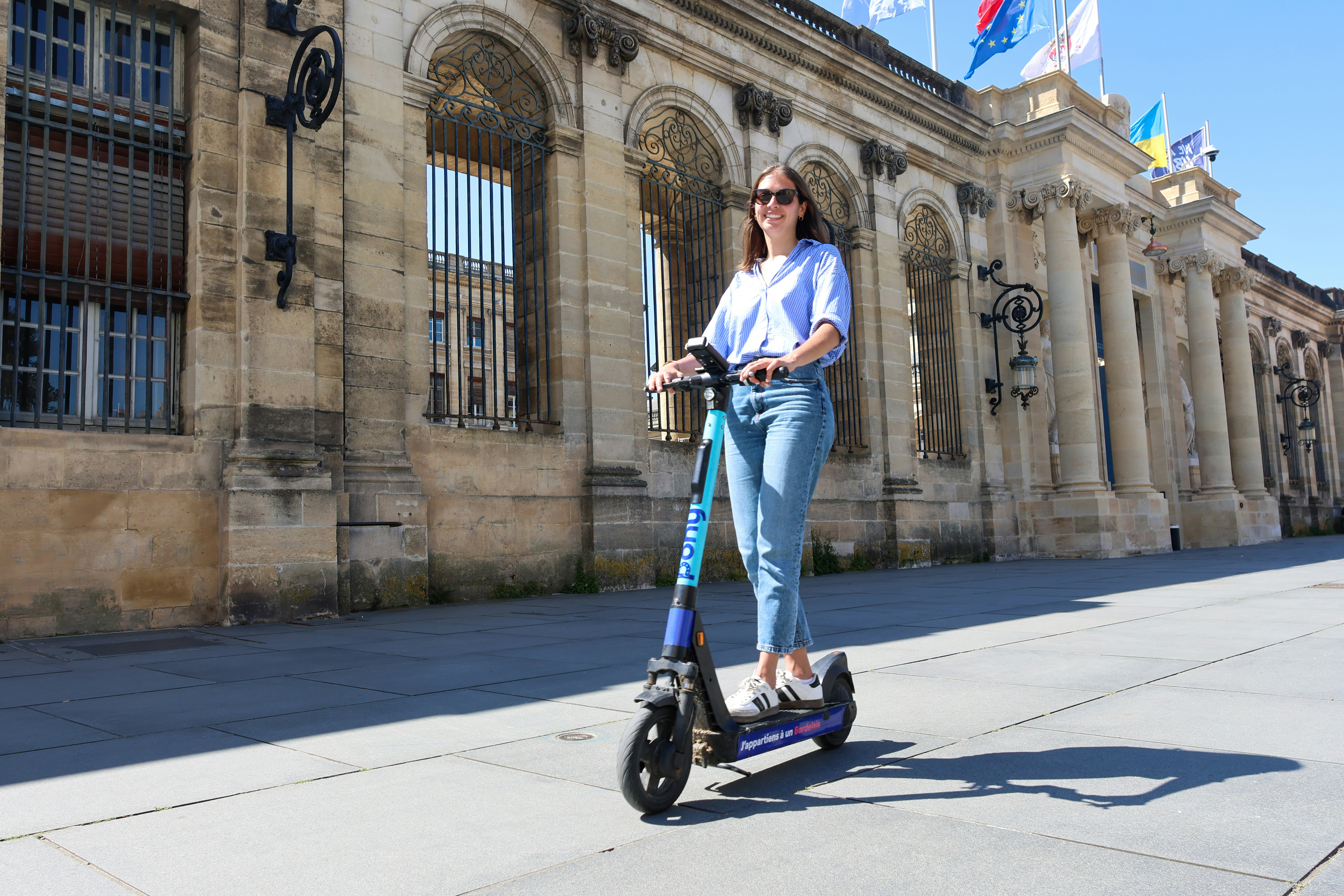 Woman rides an electric scooter near a stone building.