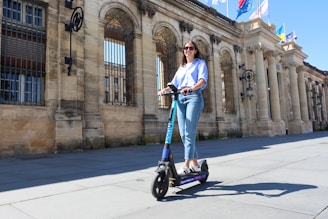 Woman rides an electric scooter near a stone building.
