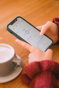 Hands hold a phone with data next to a coffee cup.