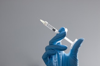 A hand in a glove holds a syringe.