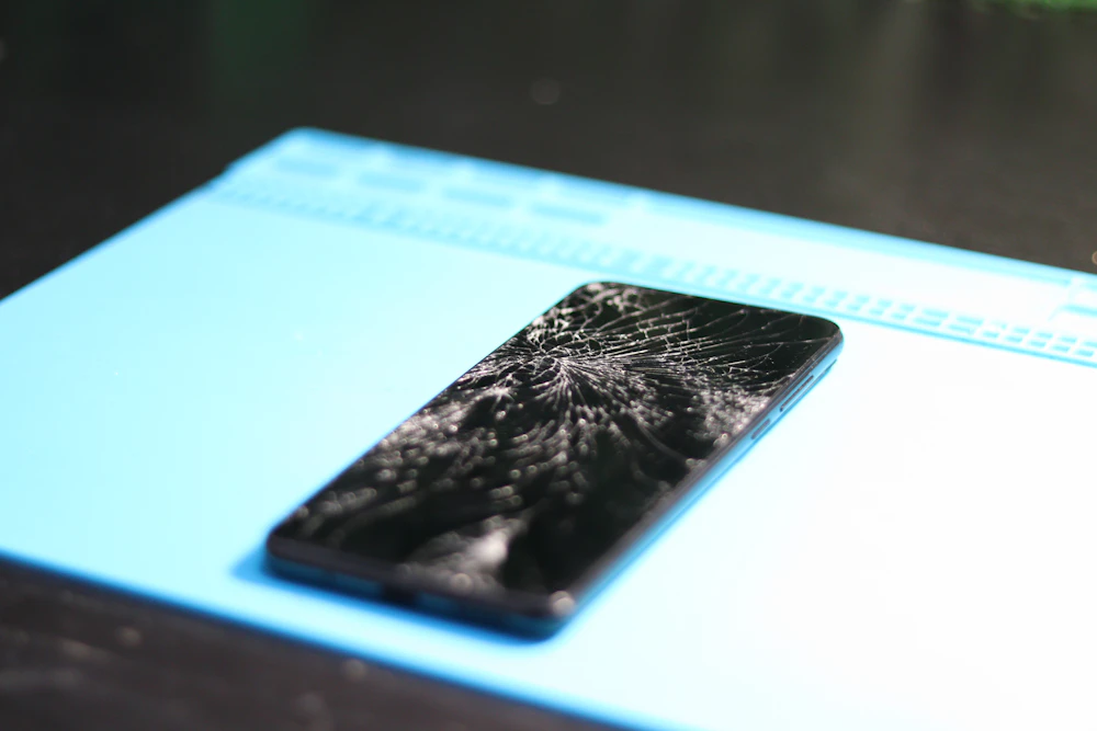 A smartphone with a shattered screen on a repair mat