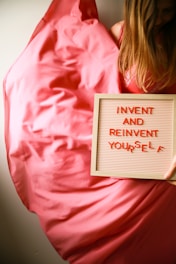 Woman holds a sign saying "invent and reinvent yourself."