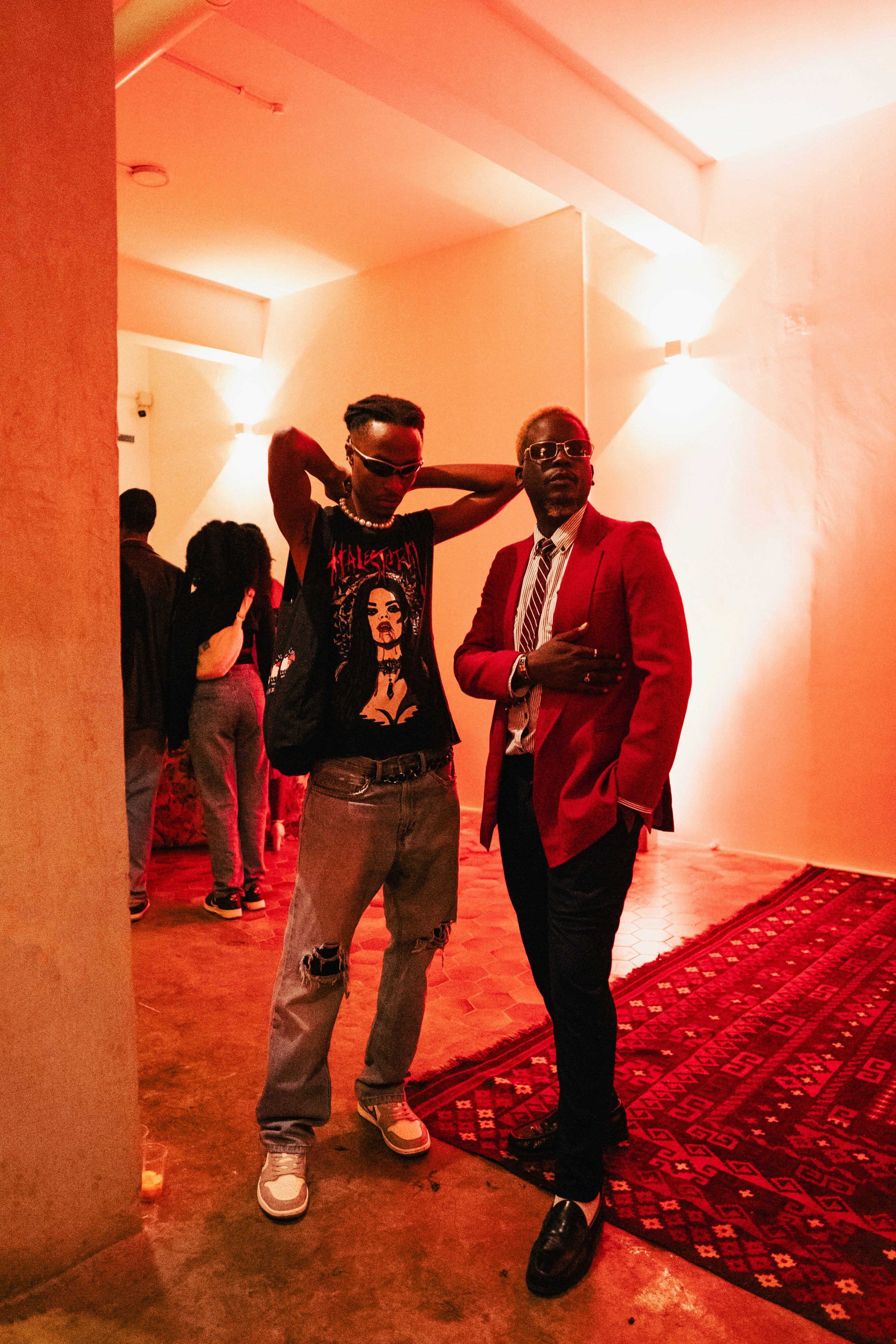 Two men pose at an event with red lighting.