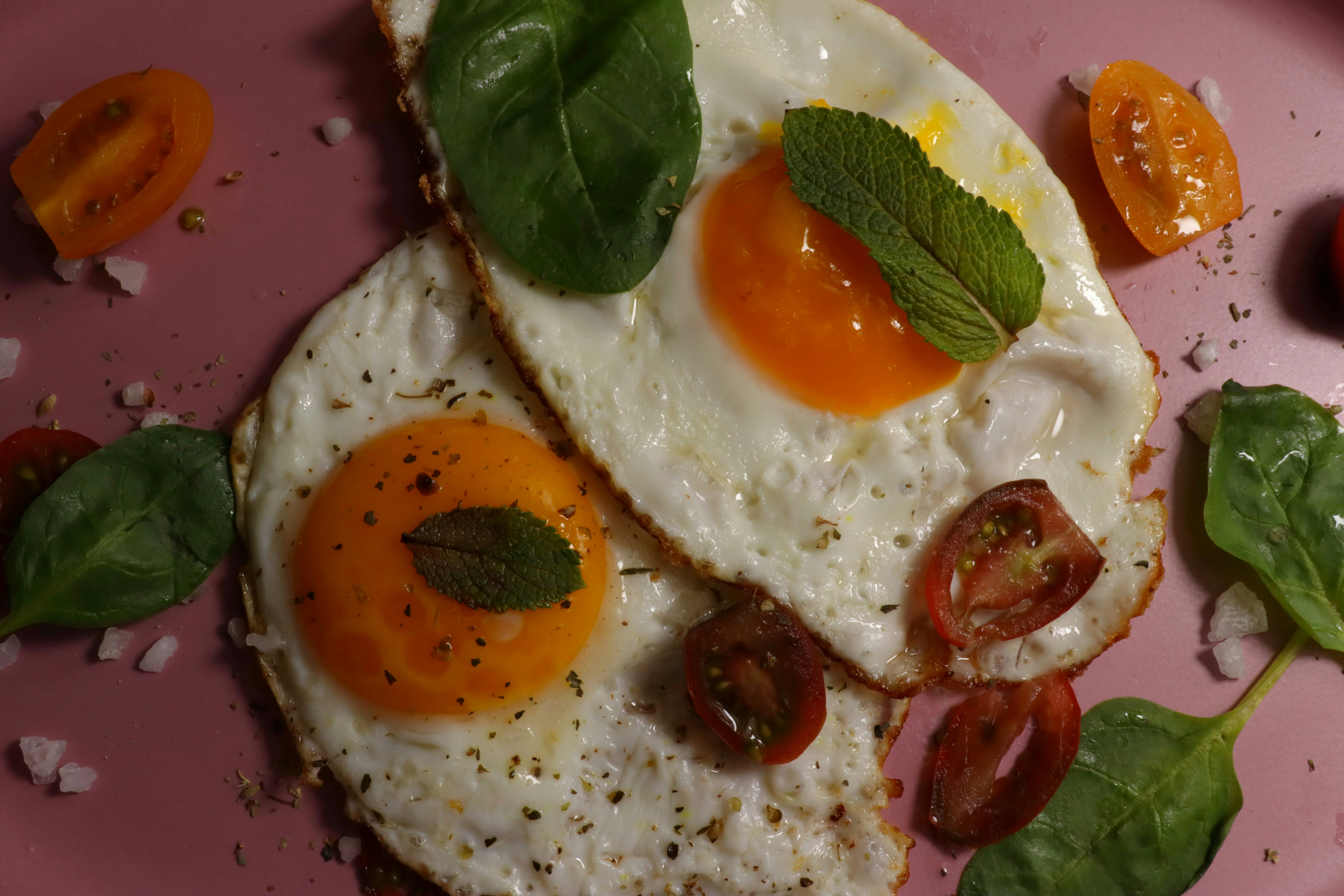 Huevos fritos y tomates en un plato rosa.