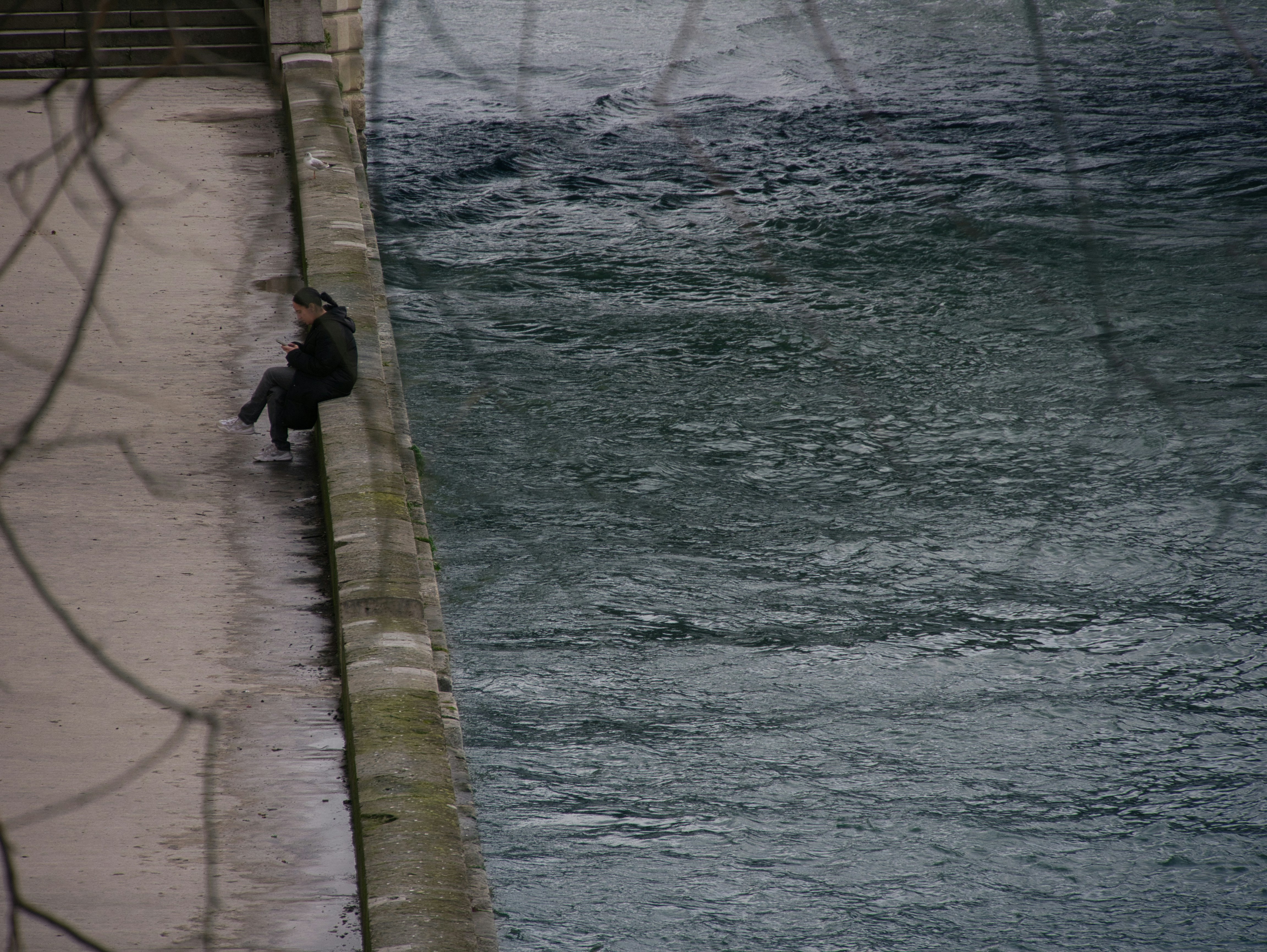 A person sits on the edge by the water.