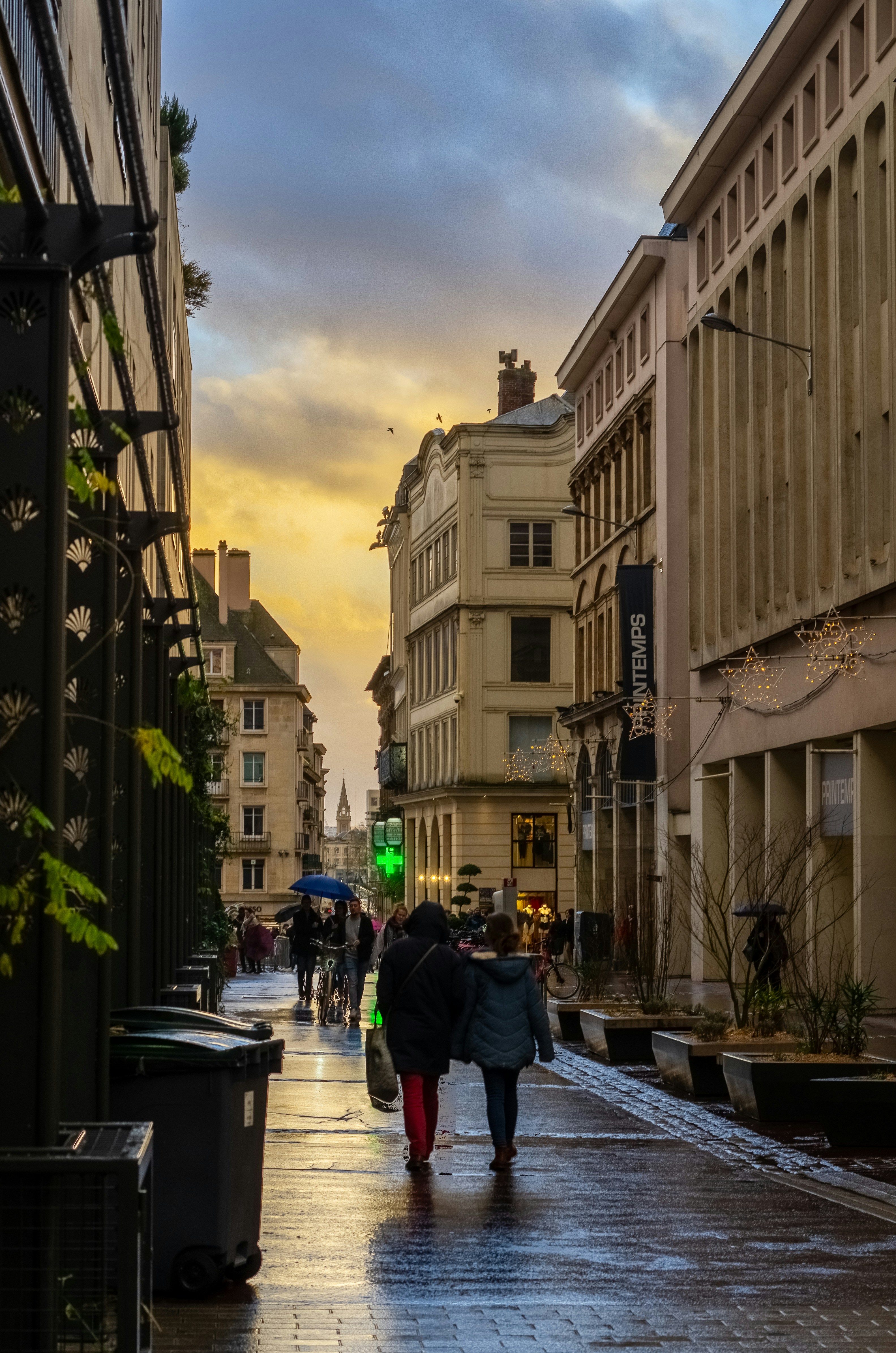 People walk down a wet street in an old city.
