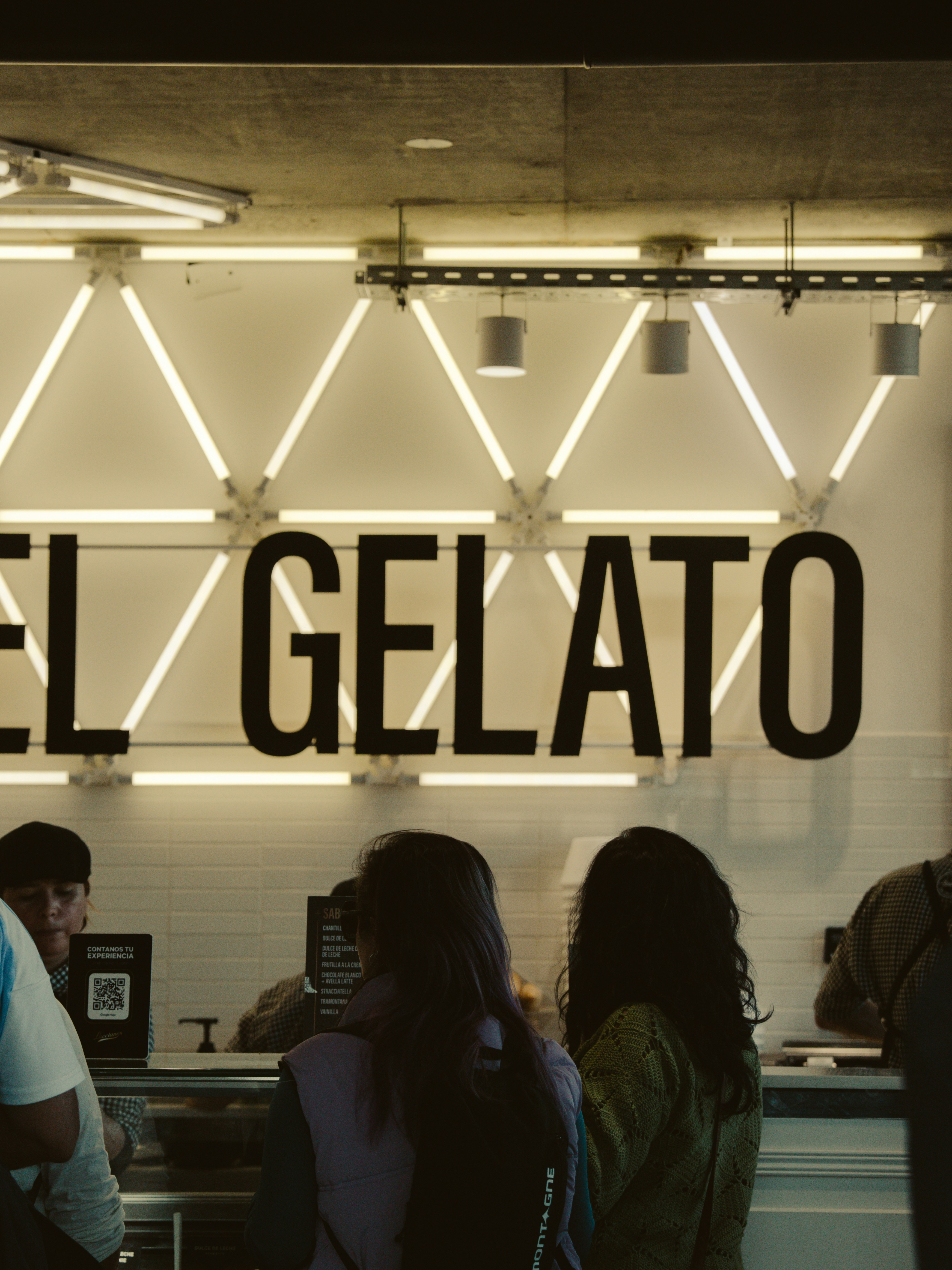 Clienti in coda al bancone di una moderna gelateria.