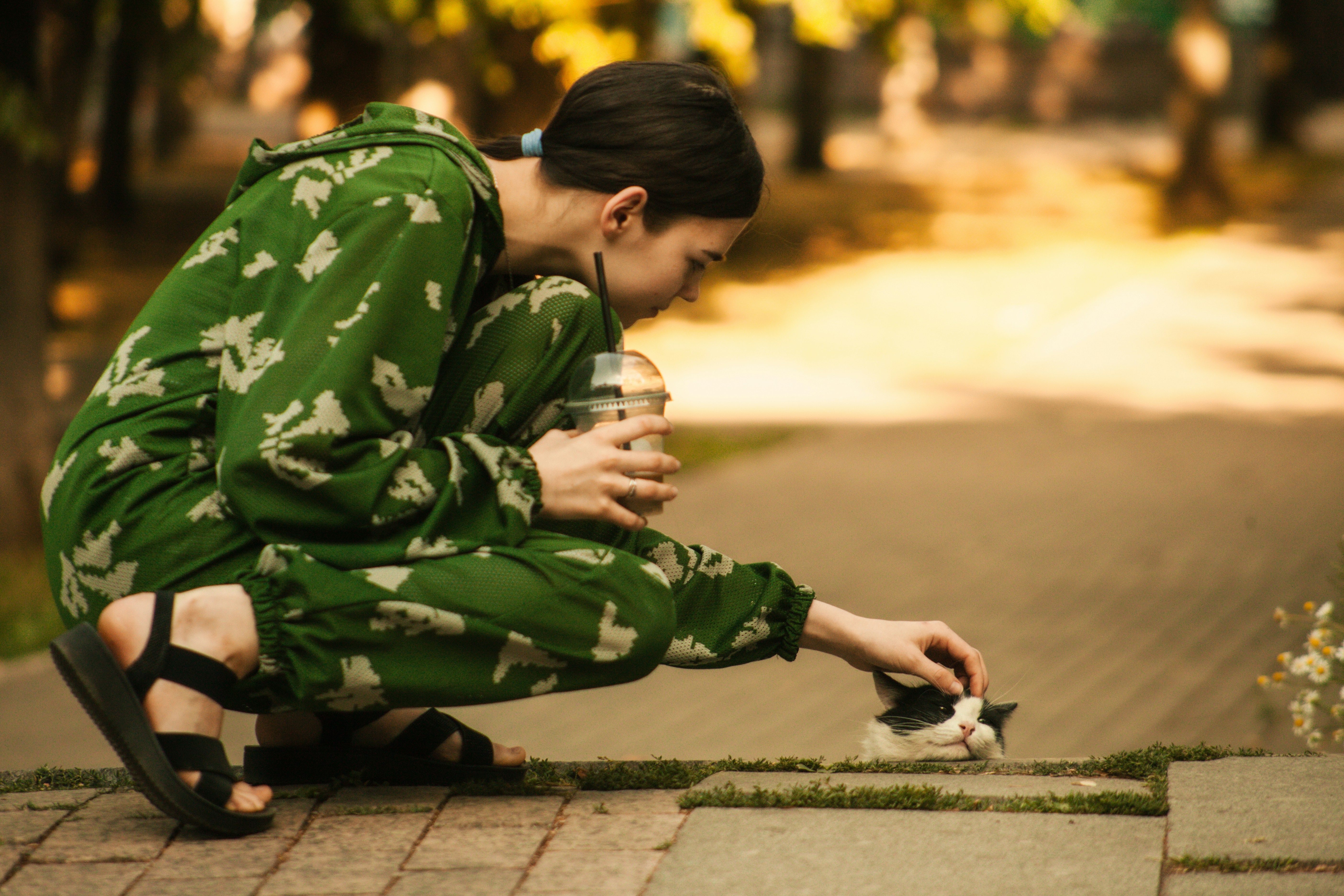 A woman petting a cat on the sidewalk.