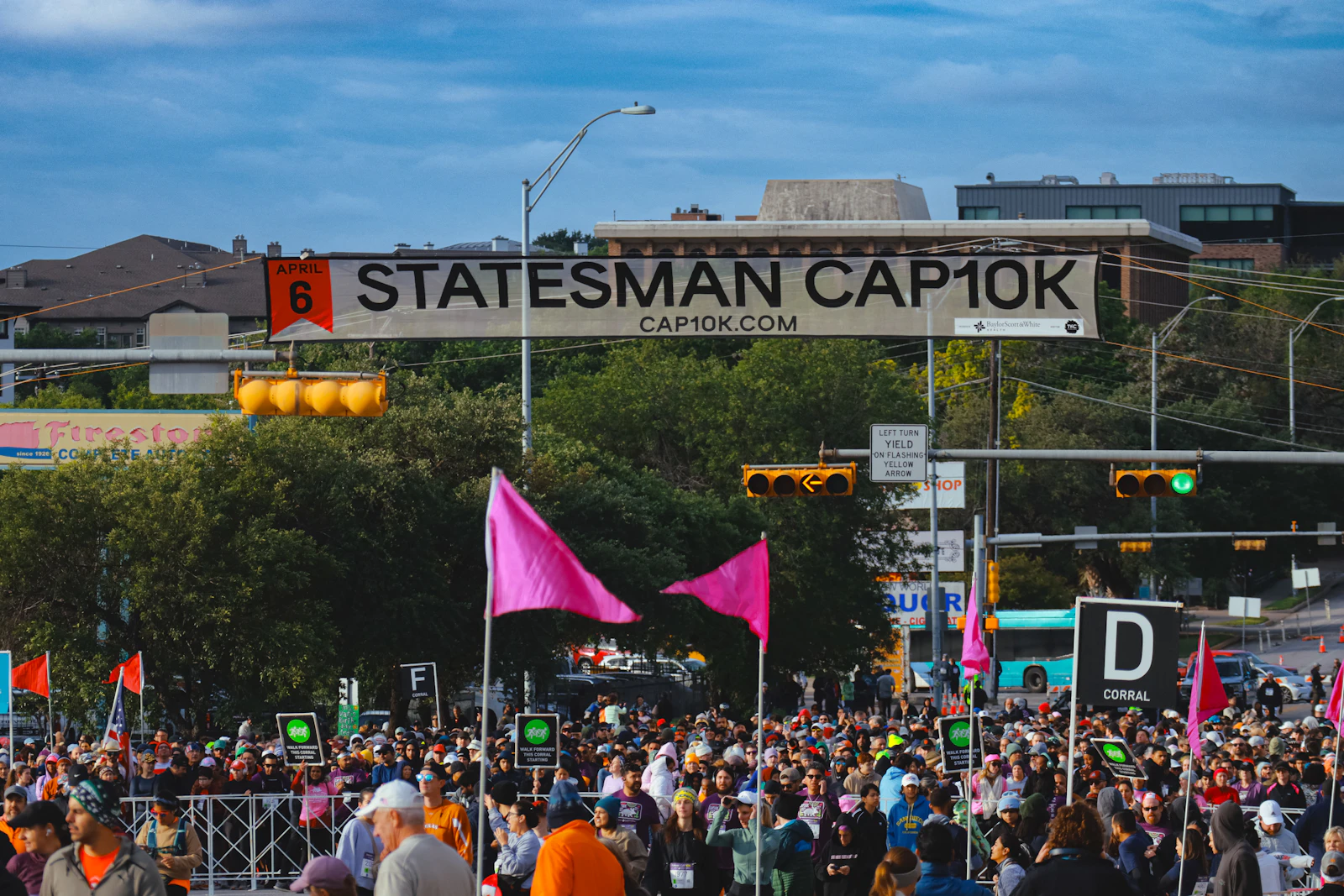 Vibrant crowd of runners gathered at the starting line of a 5K race with bright pink flags and event banners overhead