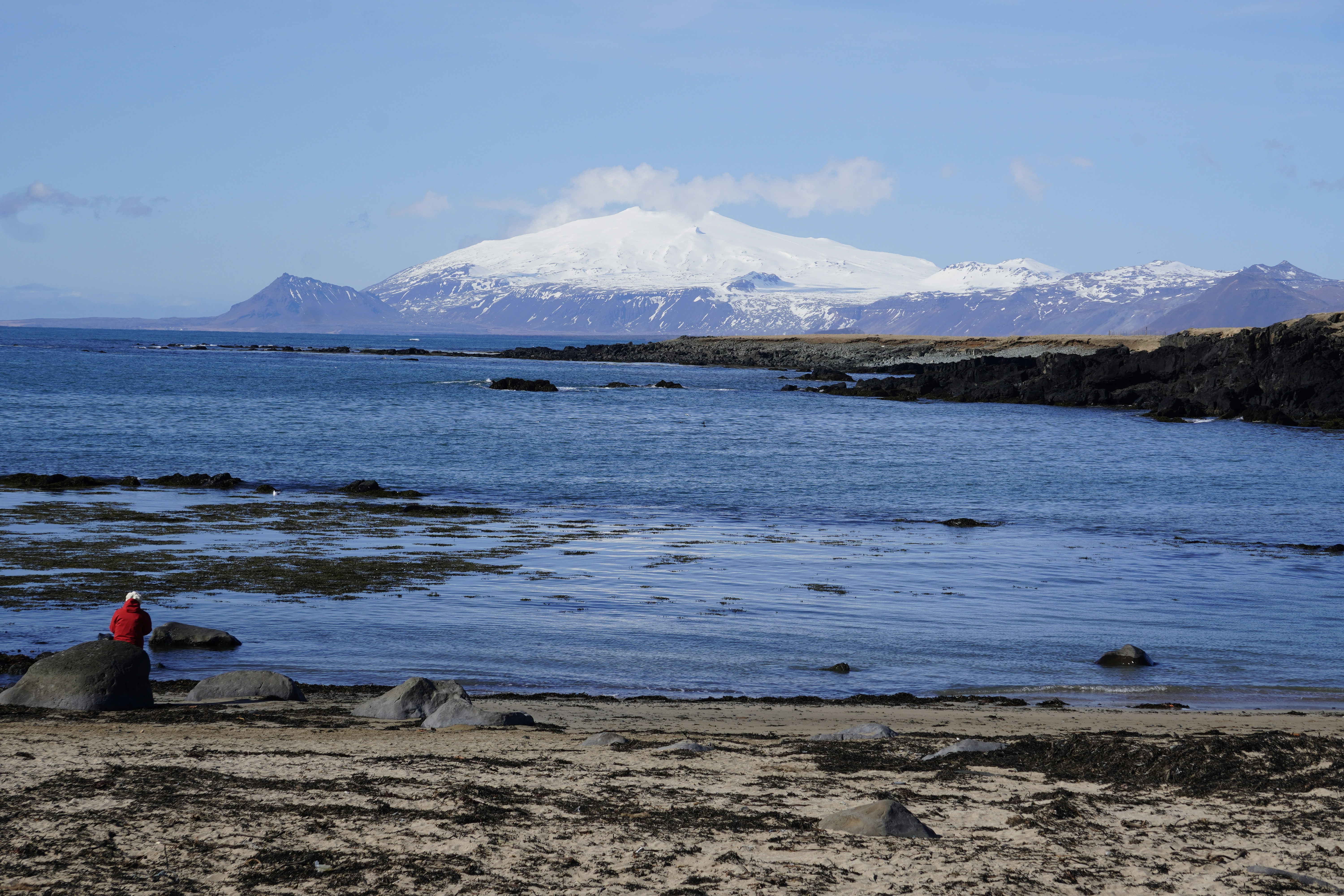 Person sits by the sea, mountain in background