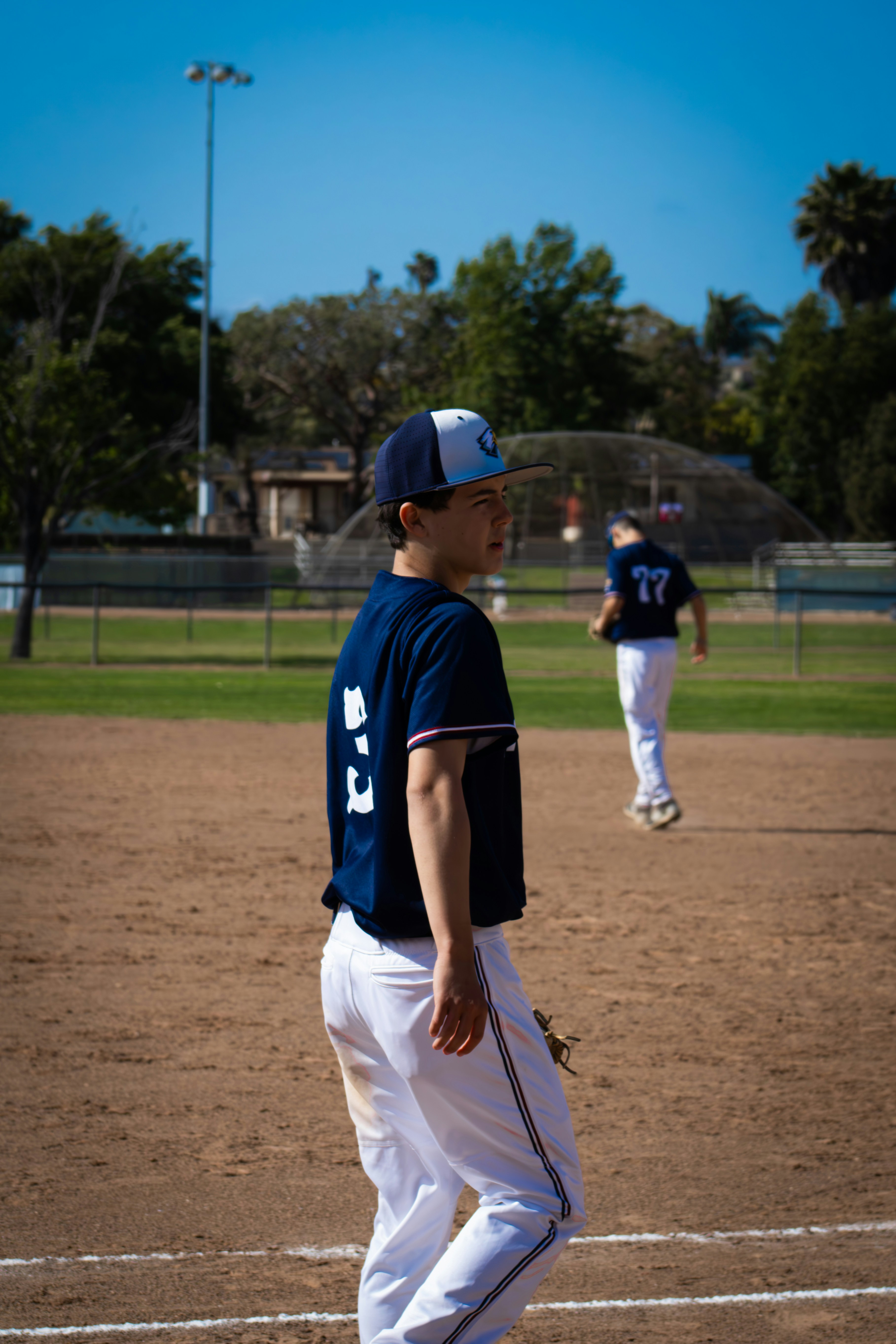 Baseball players are on the field, in the sun.
