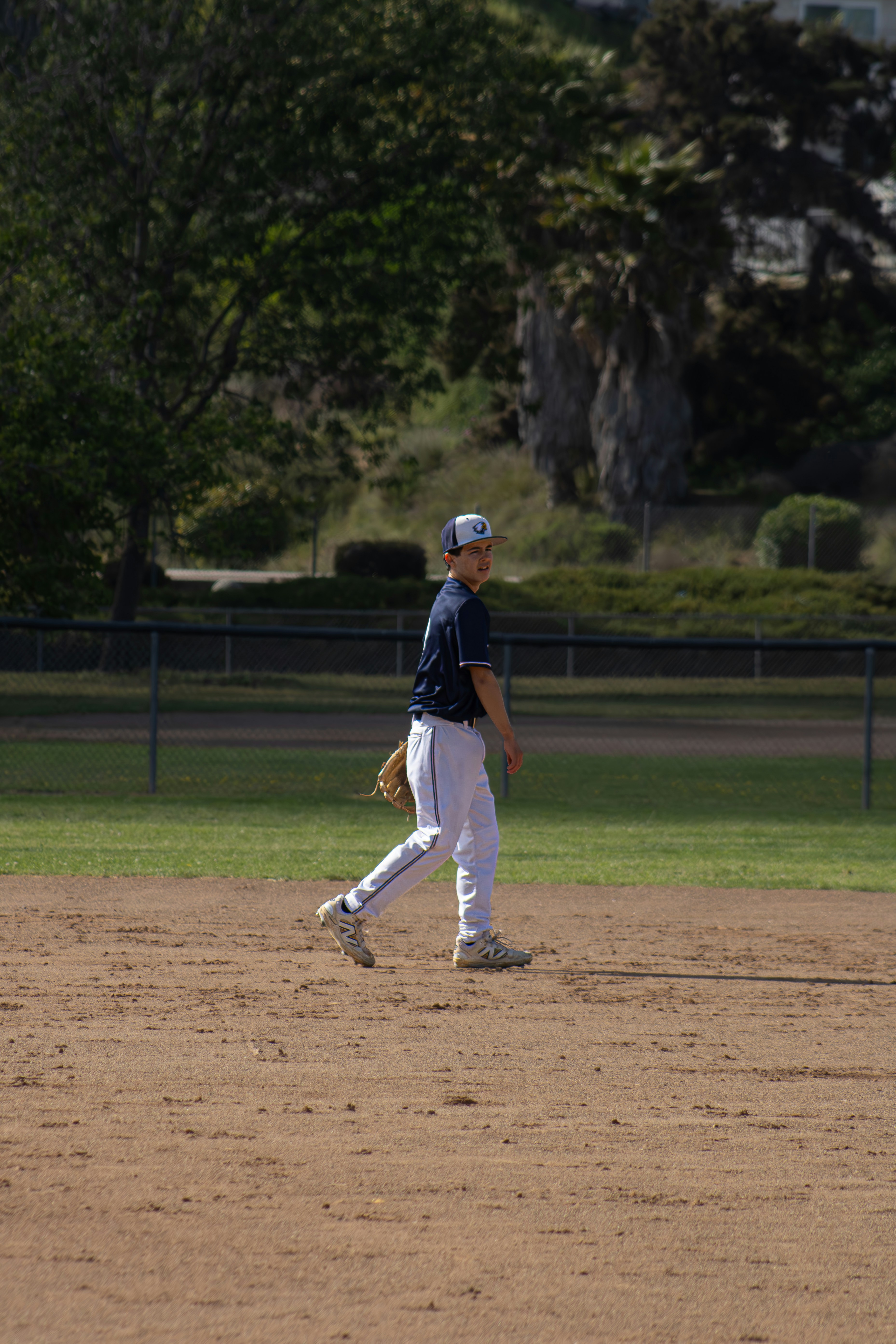 A baseball player walks on a dusty field.