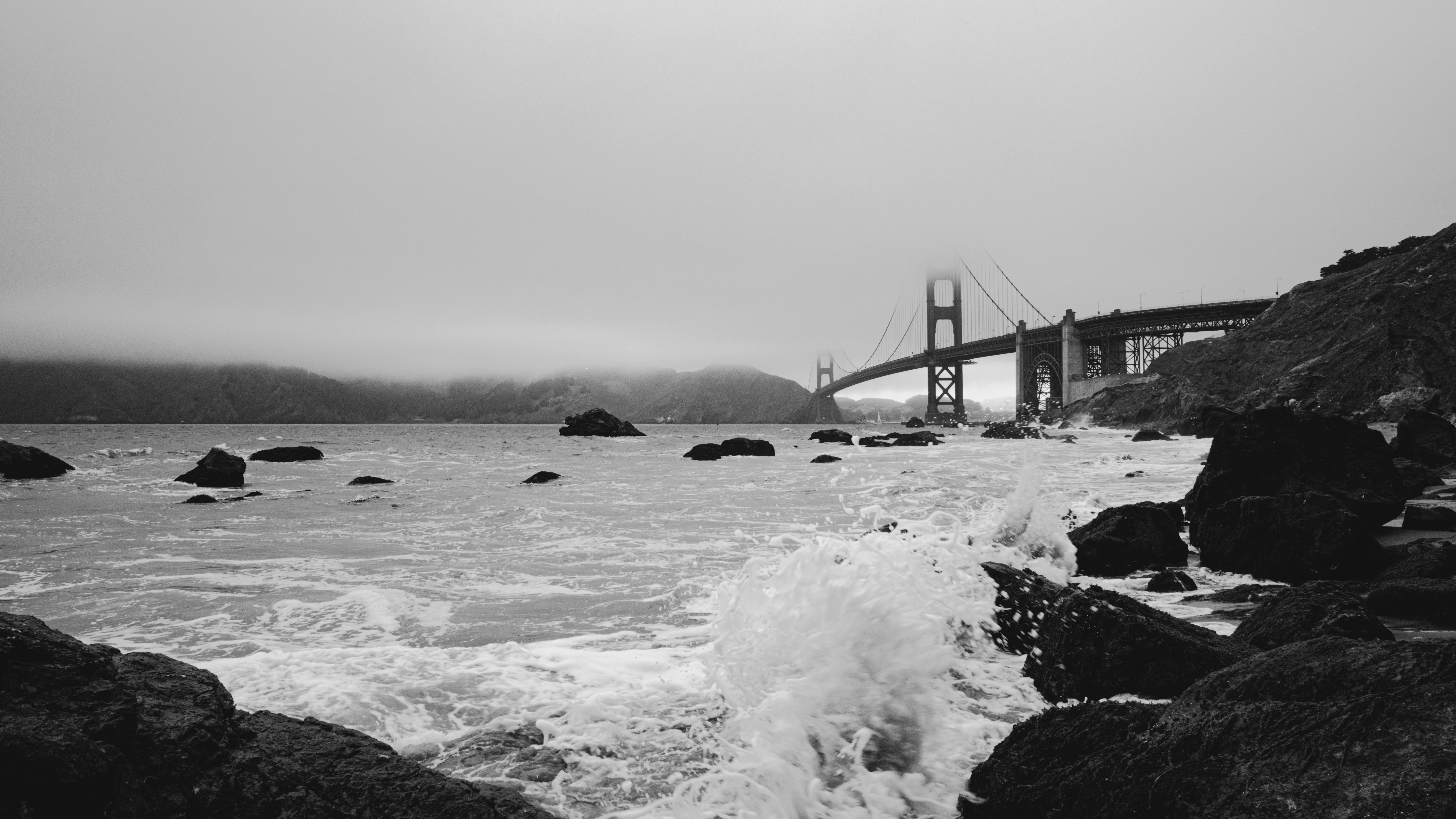 Golden gate bridge sits by the sea in grayscale.