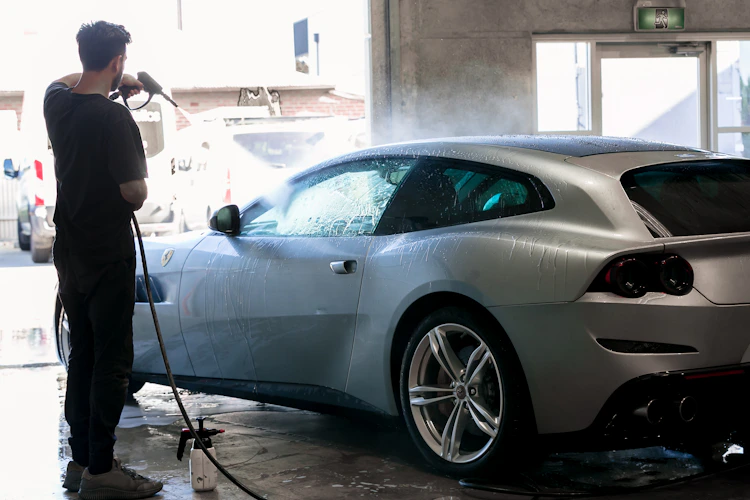 Man washes a silver car in a car wash.