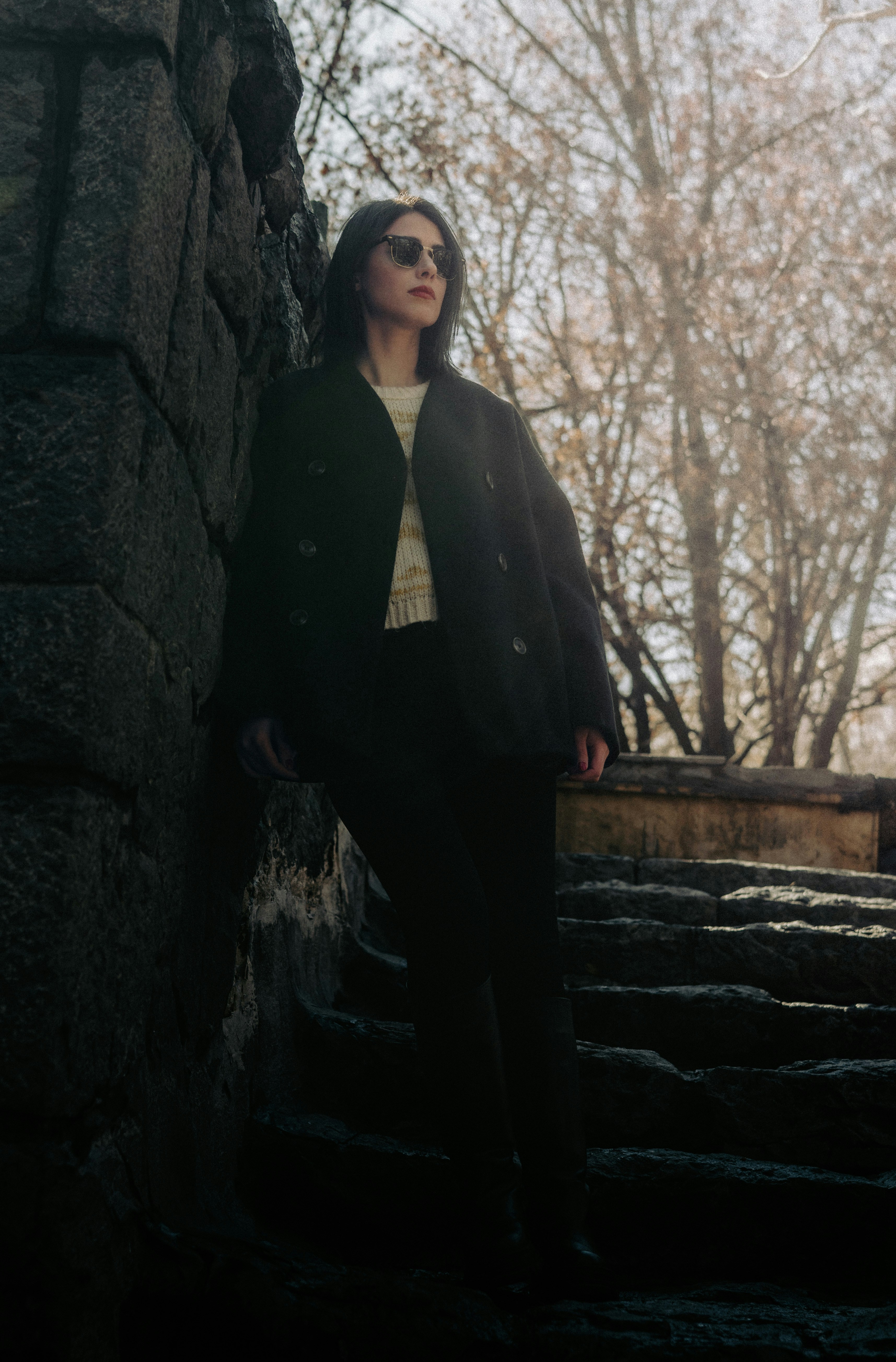 A stylish woman poses next to a stone wall.