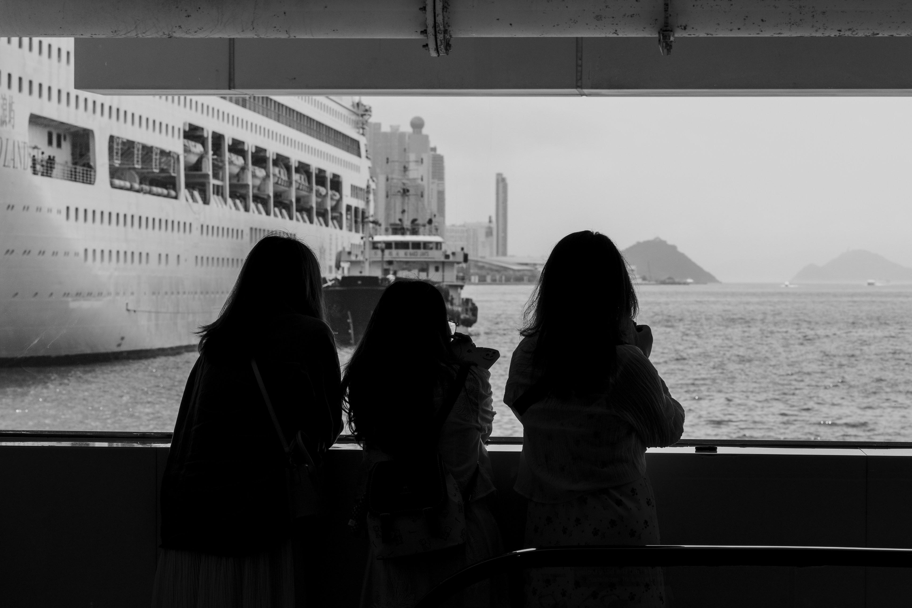 Three people watch a ship from a pier.
