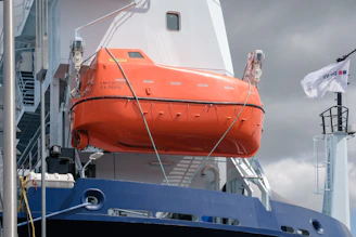 An orange lifeboat is attached to a ship.