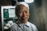 A smiling elderly man stands in front of a cabinet.
