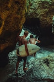 Surfers walk through the rocks into the water.