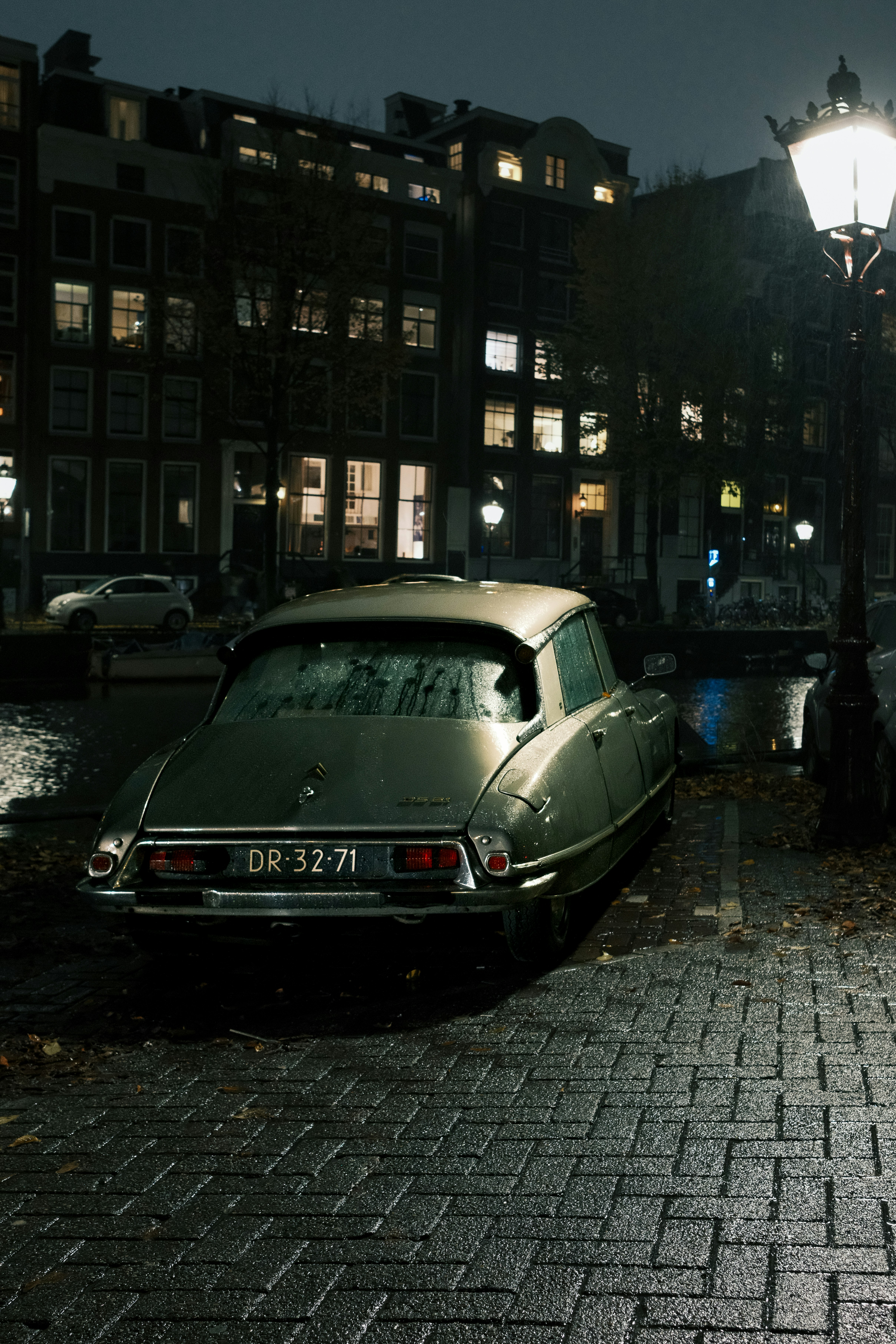 Une voiture de collection garée dans une rue pavée et humide.