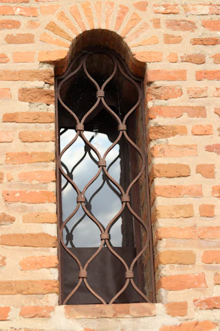 Brick wall with arched window and iron grating.