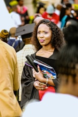 A woman in graduation attire holding books and diploma.