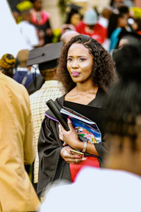 A woman in graduation attire holding books and diploma.