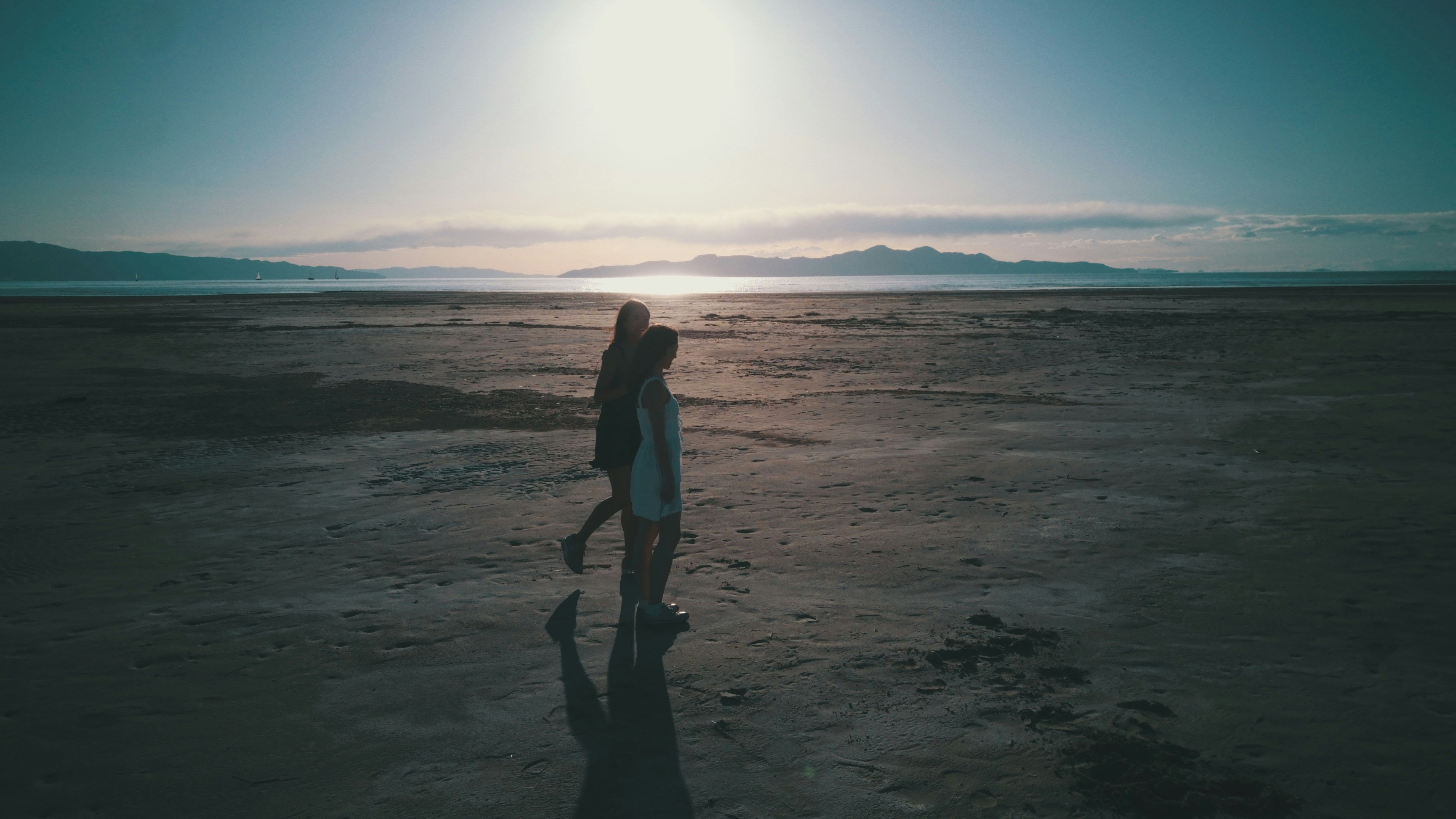 Two people walk on a beach during a sunset.