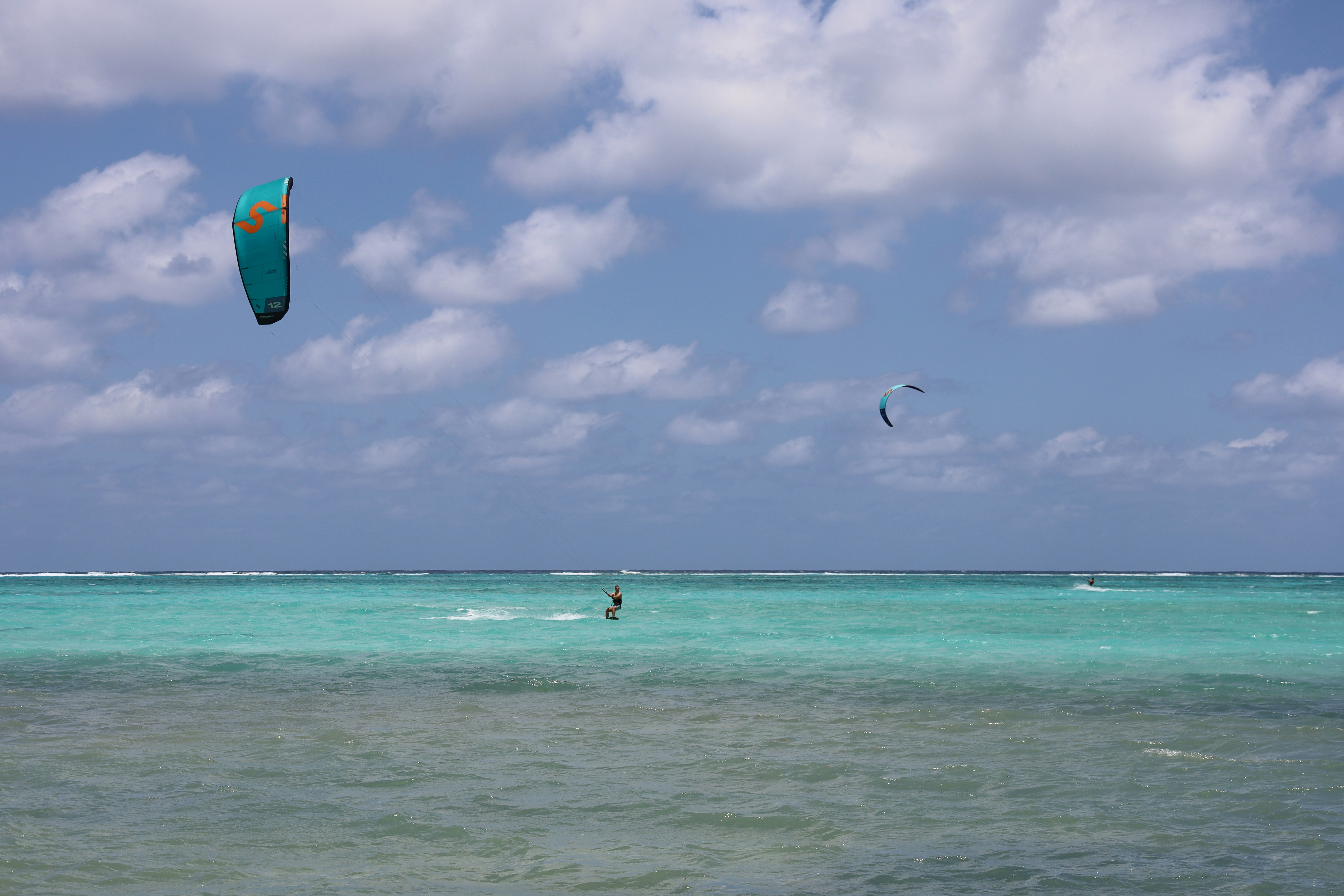 Kite surfers ride the waves under a cloudy sky.