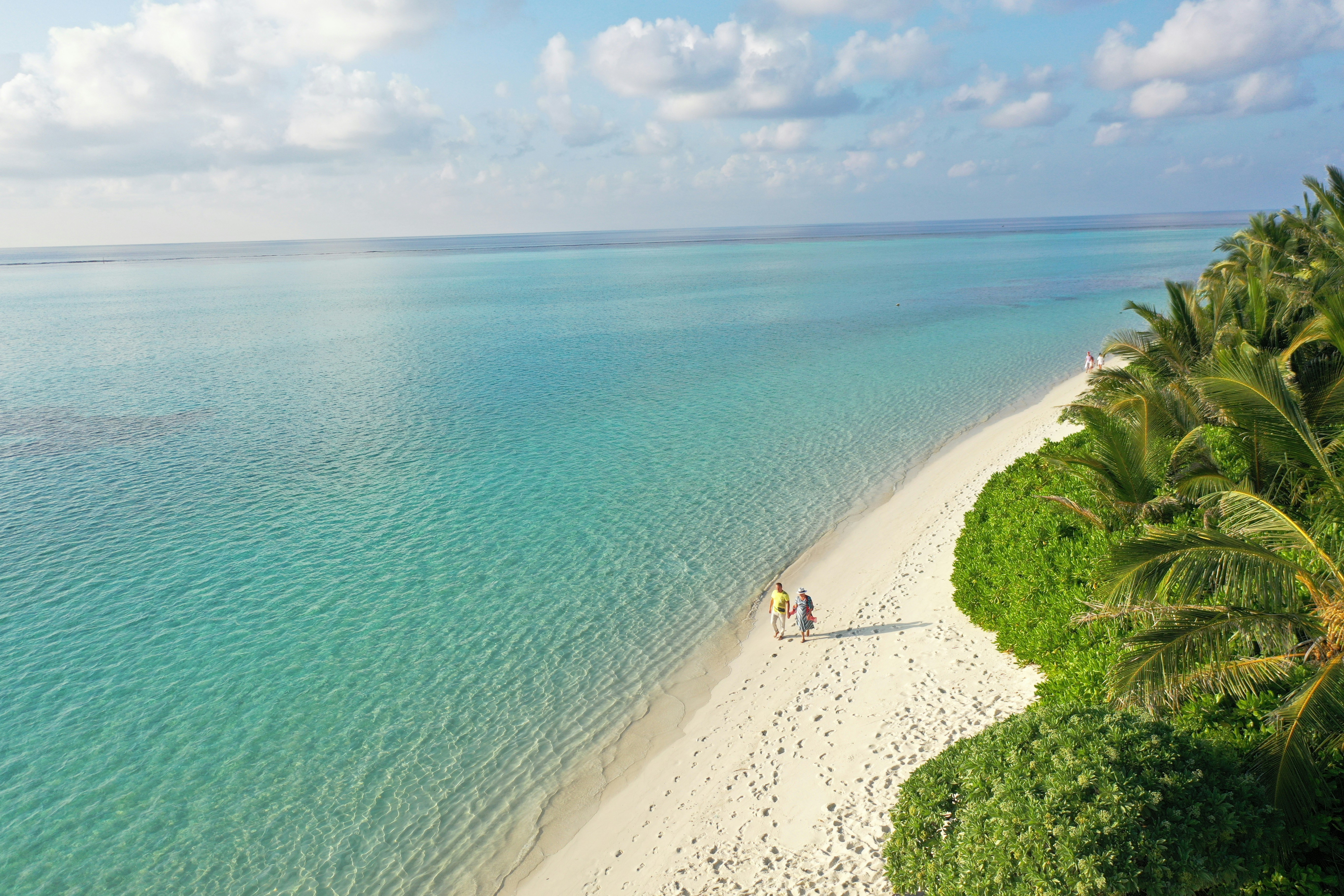 Couple walking on a tropical beach with turquoise water.