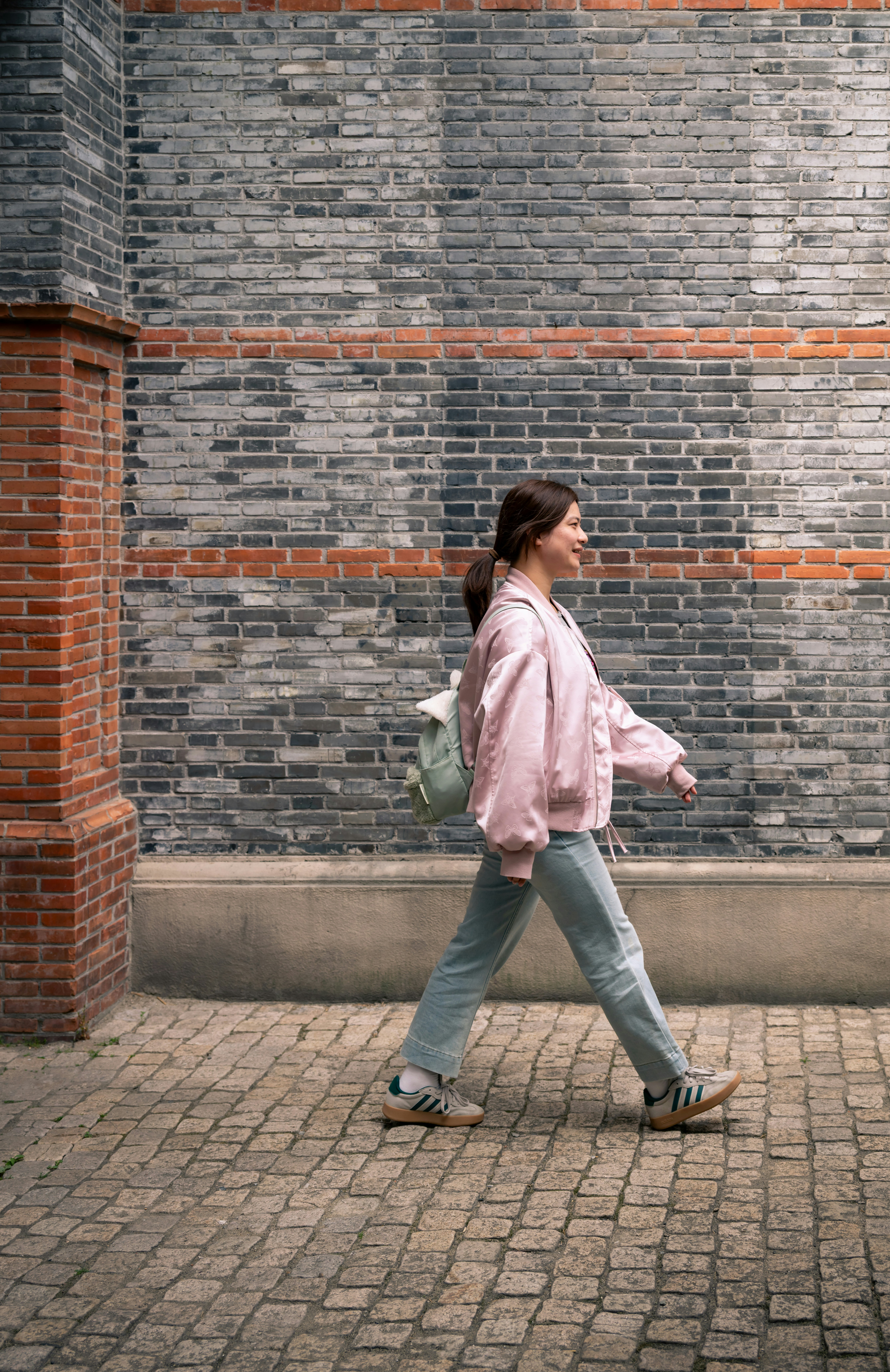 A woman walks along a brick wall.