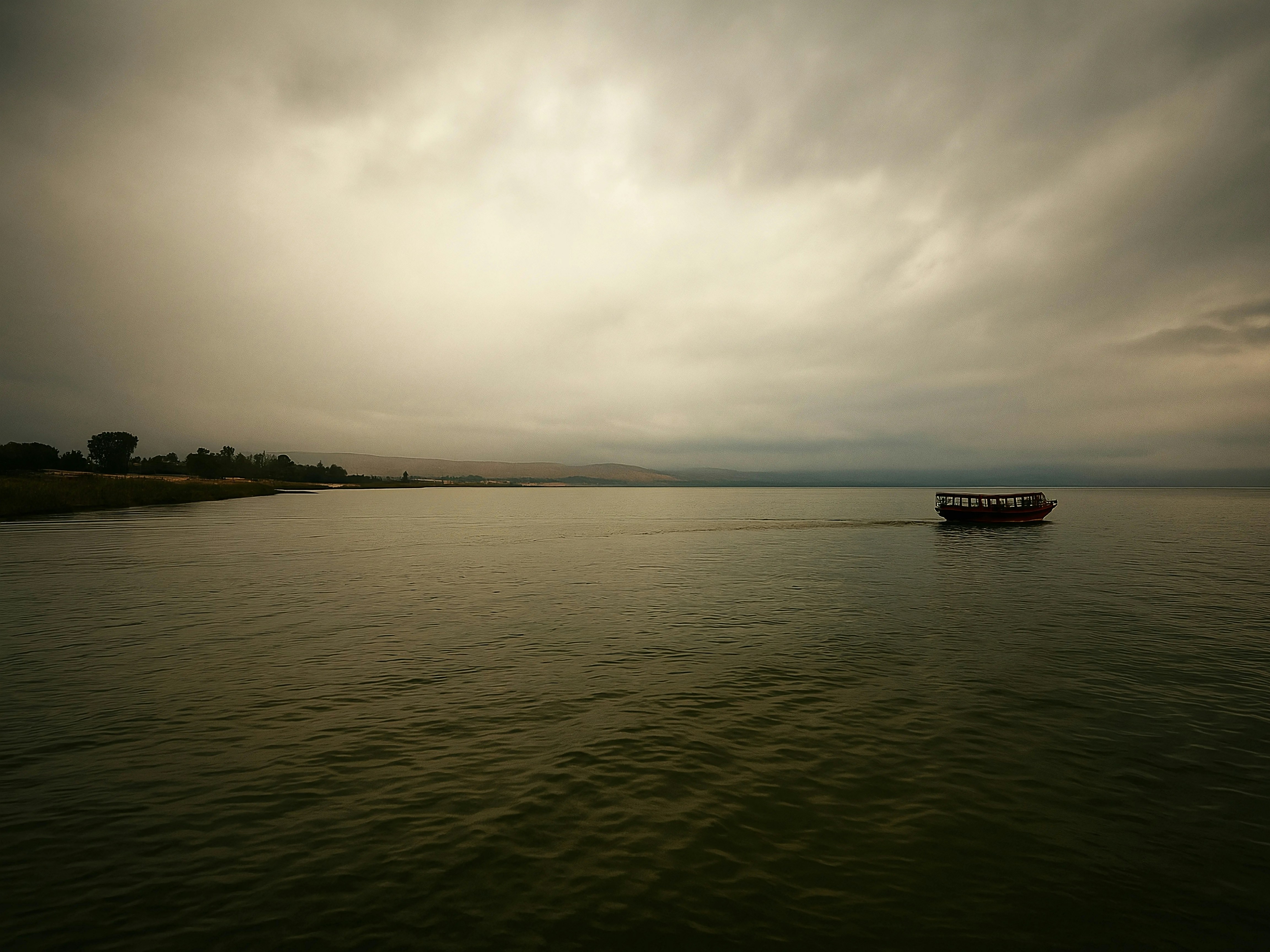 A boat sails on calm water under a cloudy sky.