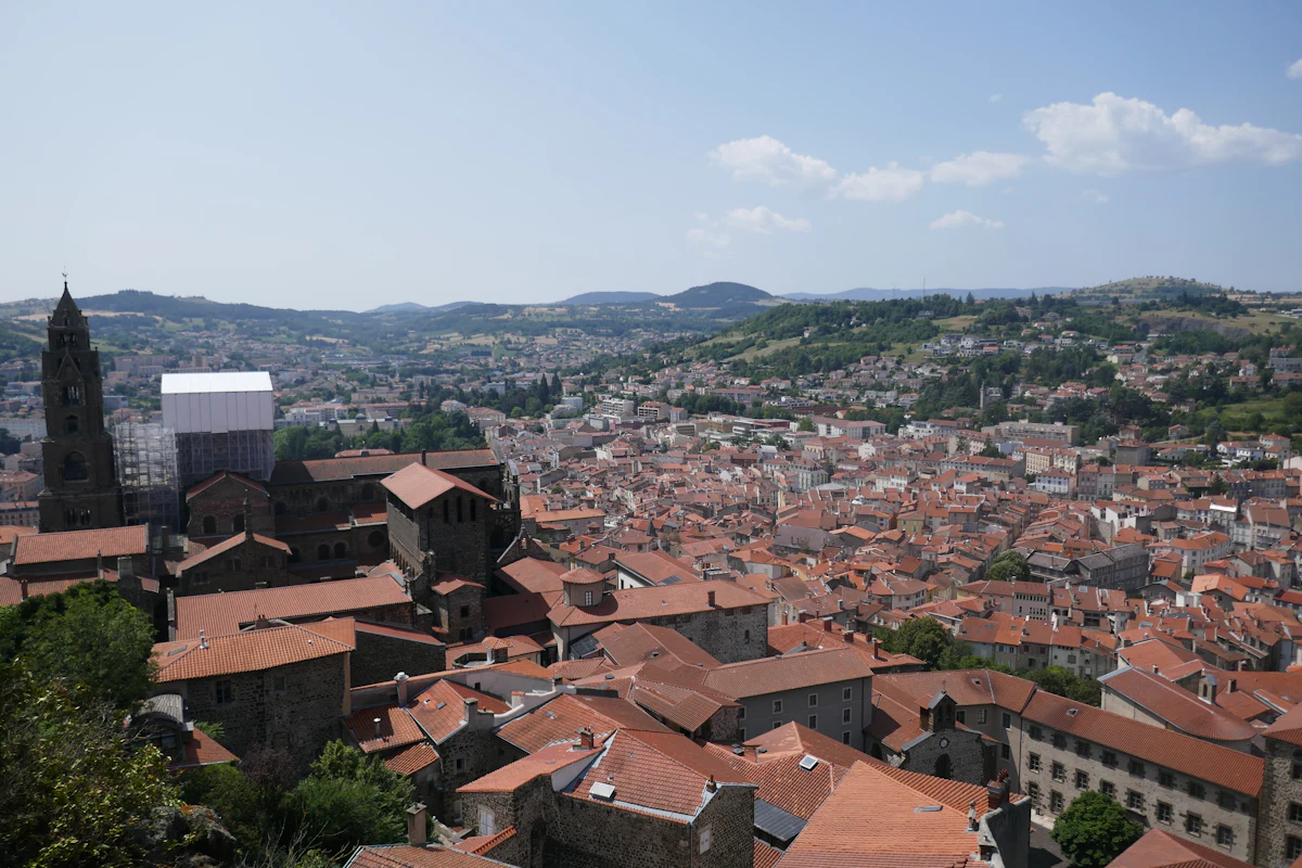 Red tile roofs of Le Puy-en-Velay and the cathedral bell tower, with green hills behind