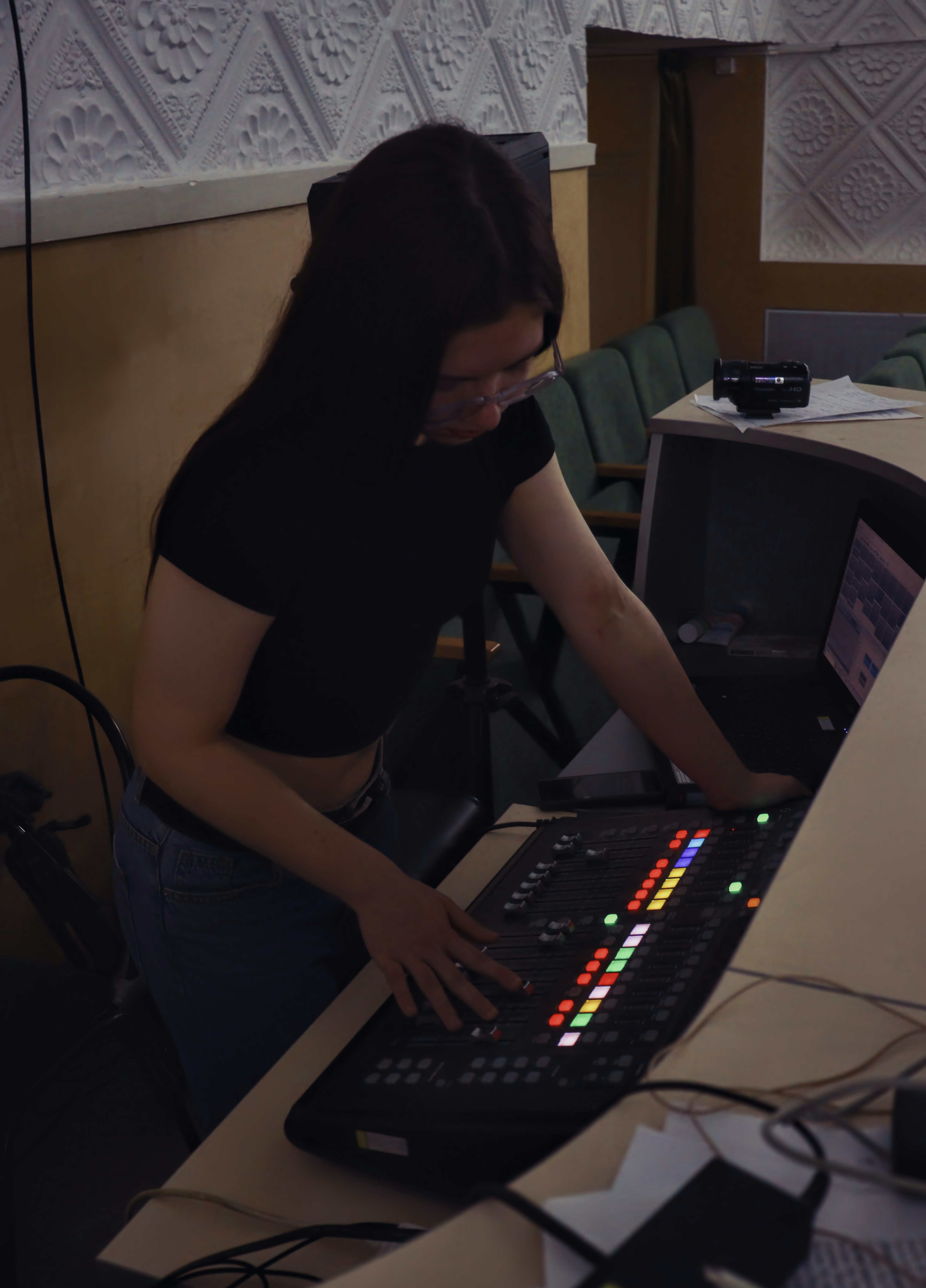 A woman works a soundboard in a theatre.