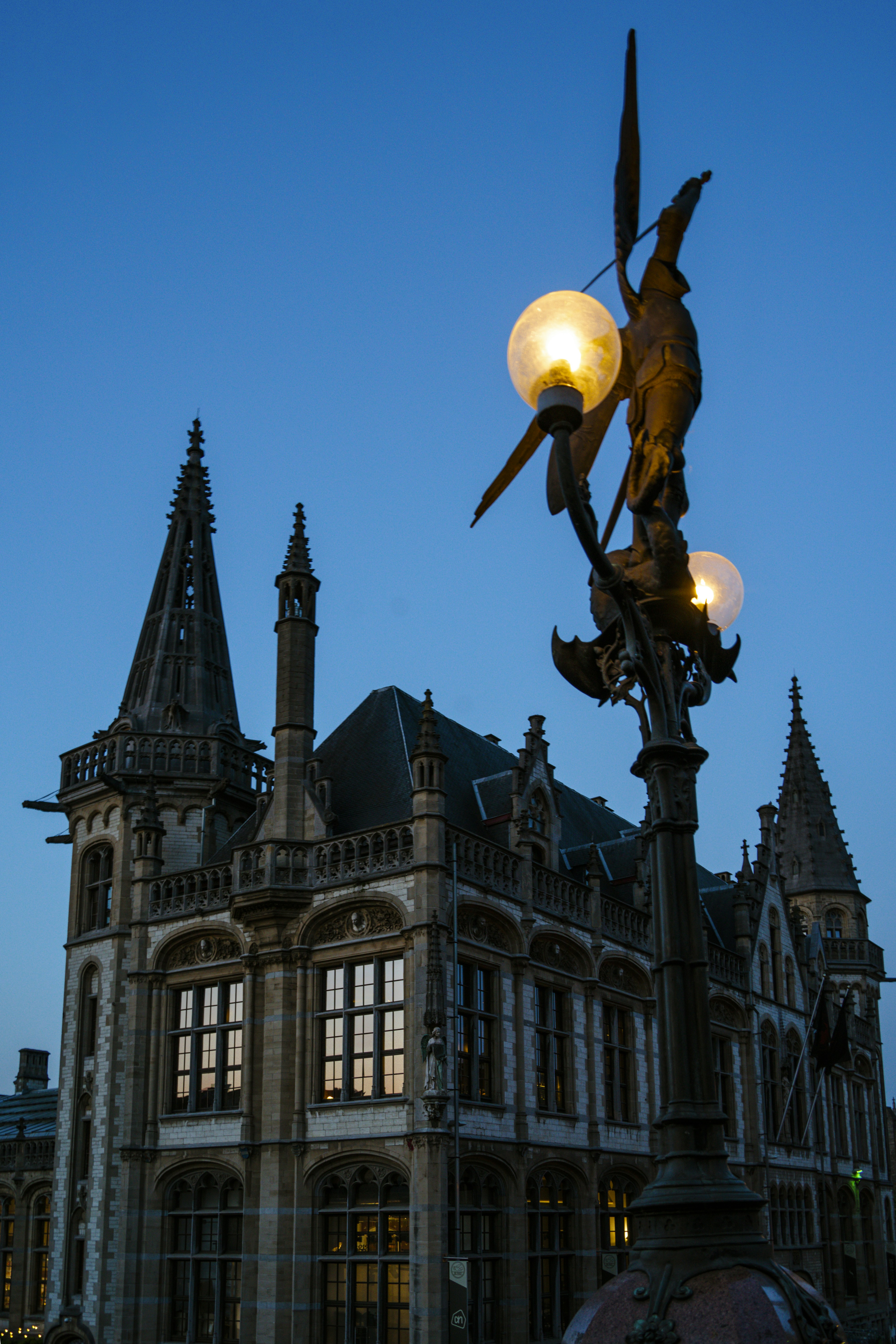 A lamp post illuminates a gothic building at dusk.
