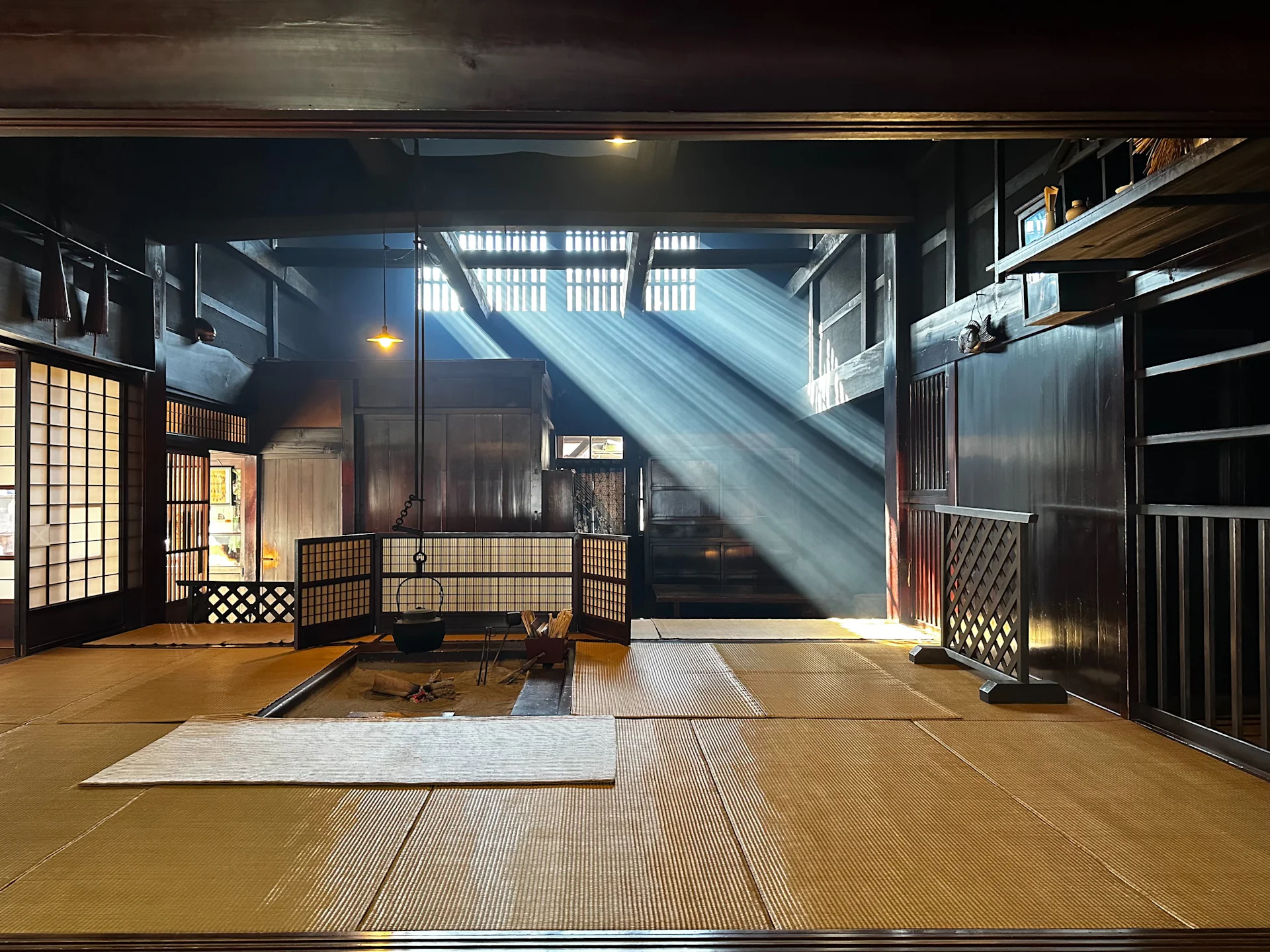 Old farmhouse interior with an irori hearth and shafts of light through smoke