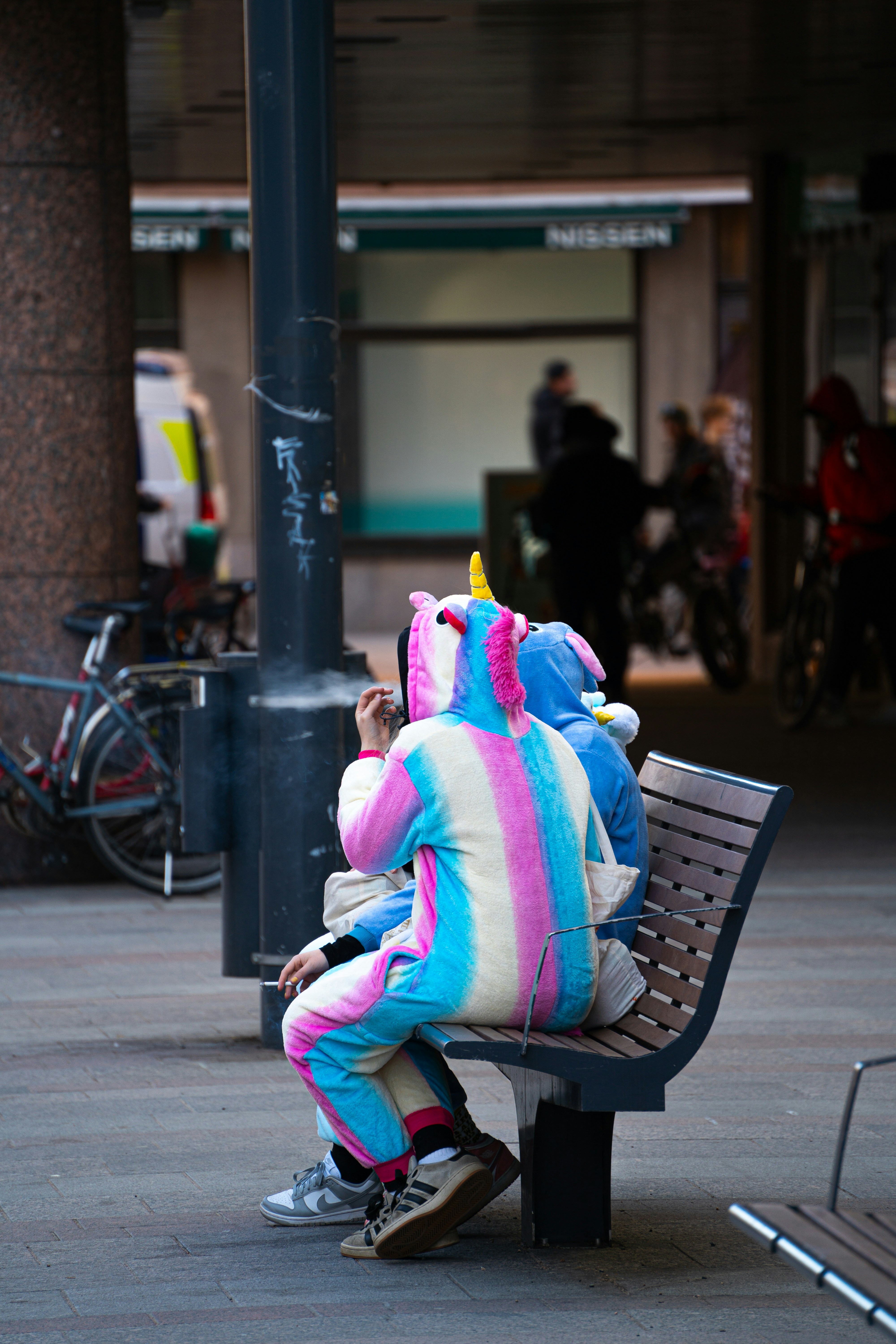 Orang-orang berkostum unicorn duduk di bangku.