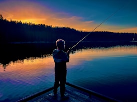 A child fishes at dusk by the lake.