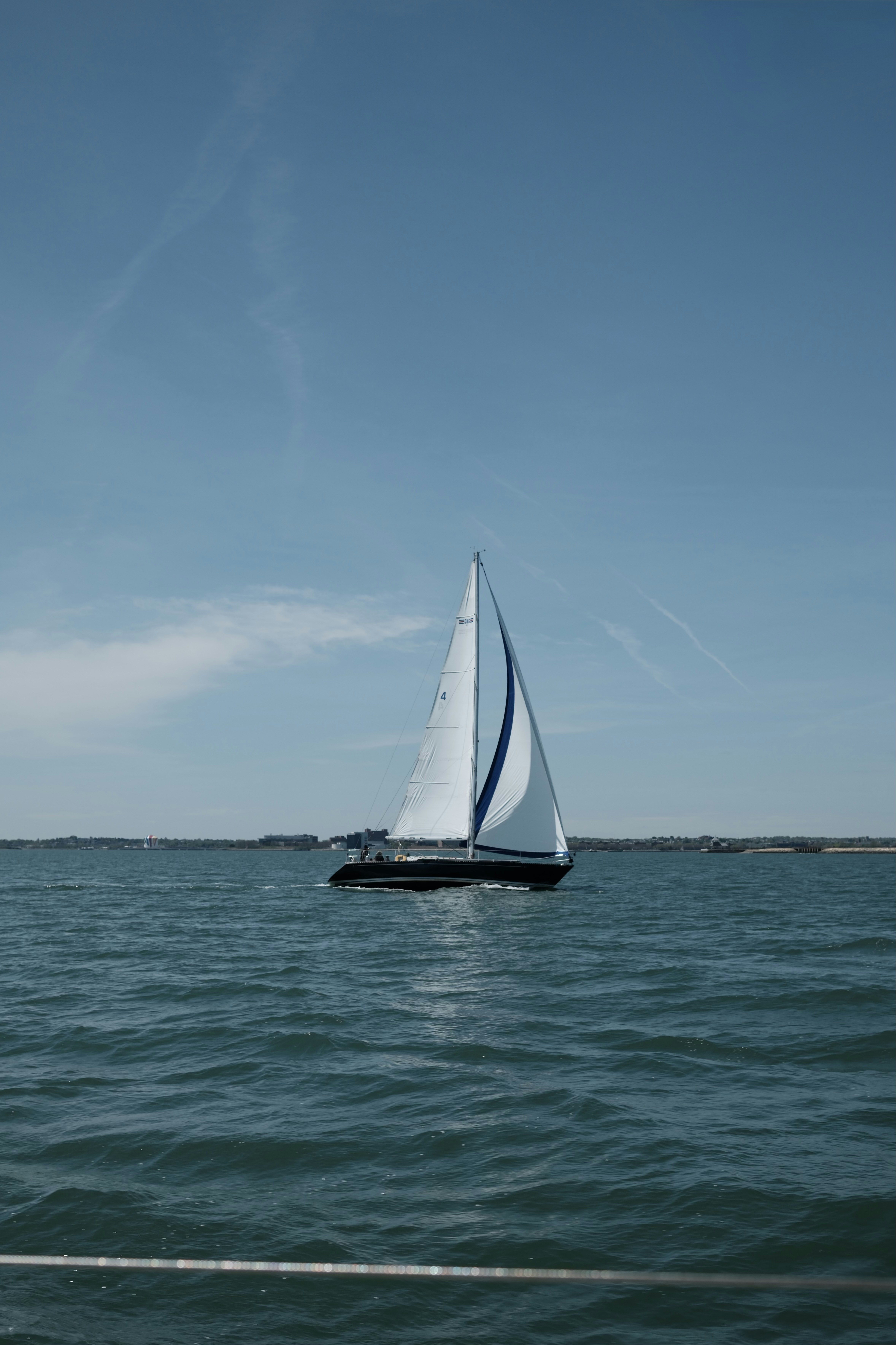 A sailboat sails on a clear, blue sea.