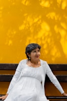 A smiling woman sits in front of a yellow wall.
