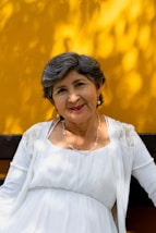 A woman smiles radiantly in front of a yellow wall.