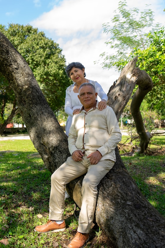 An elderly couple poses outdoors on a tree.
