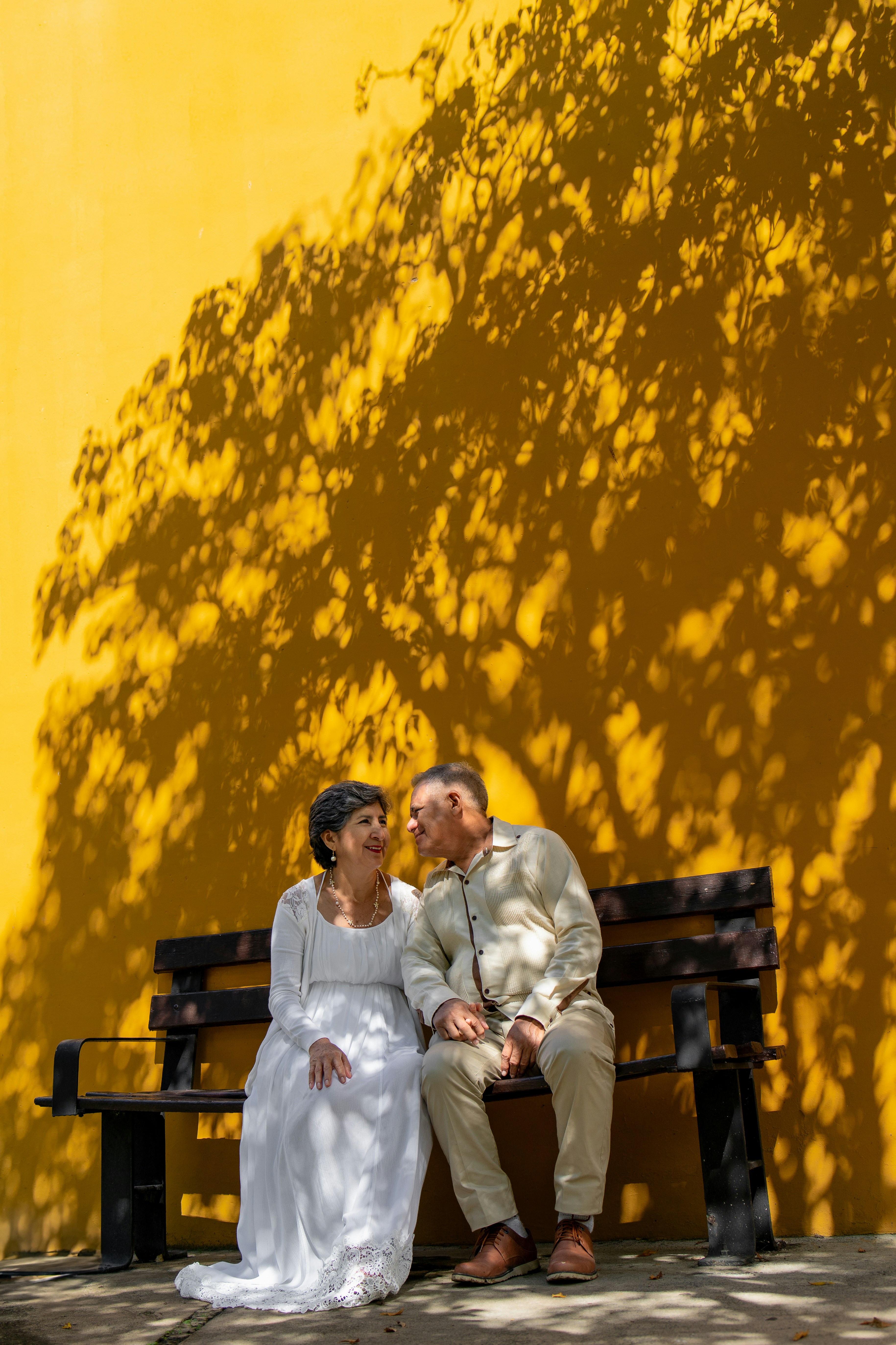 A couple sits on a bench in front of yellow.