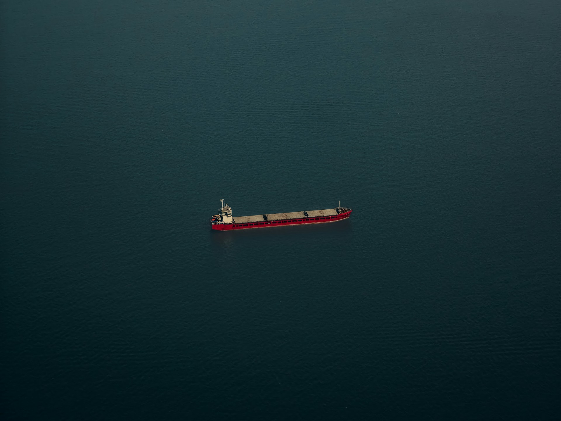 A red cargo ship floats alone at sea.