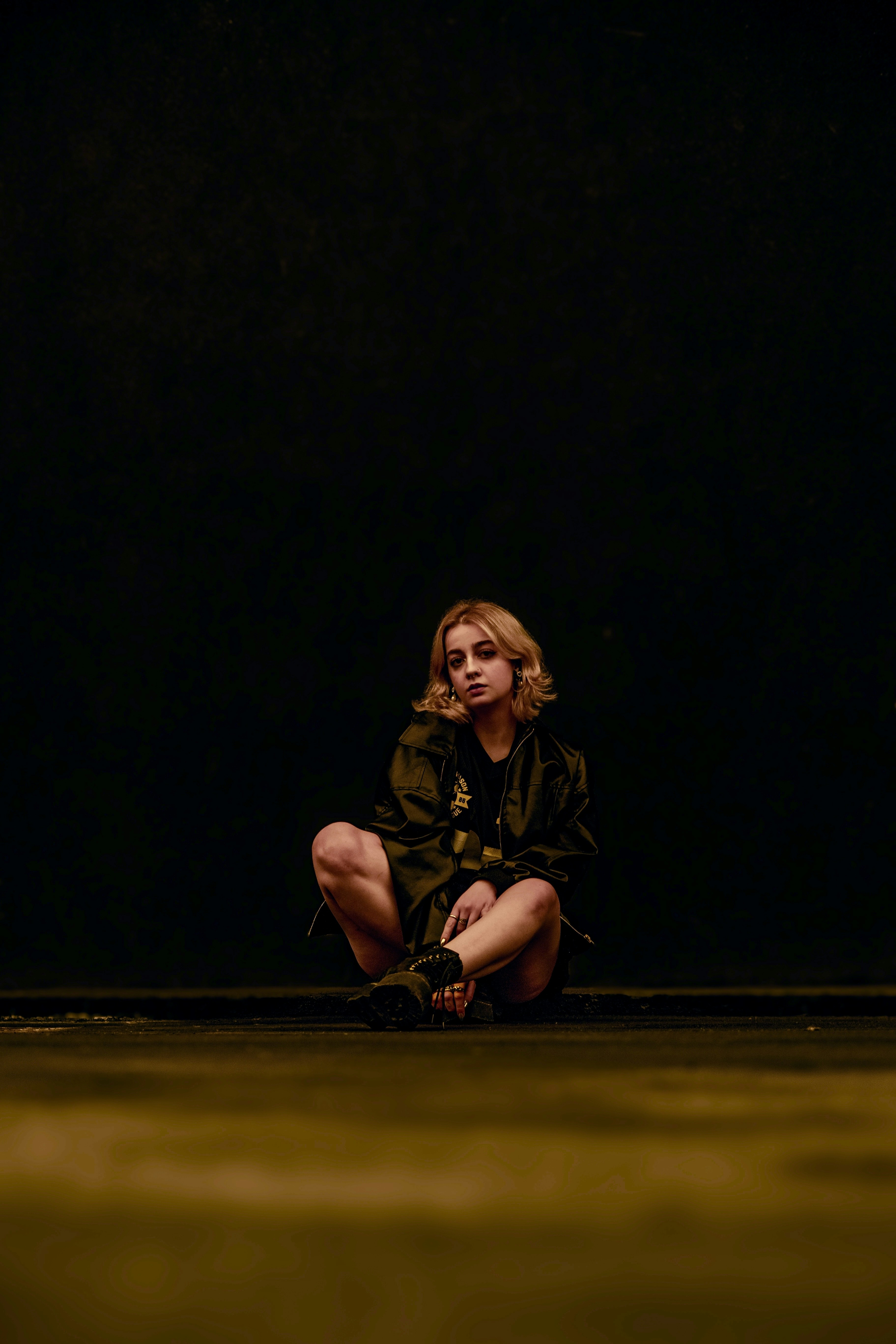 A woman is sitting alone against a black background.