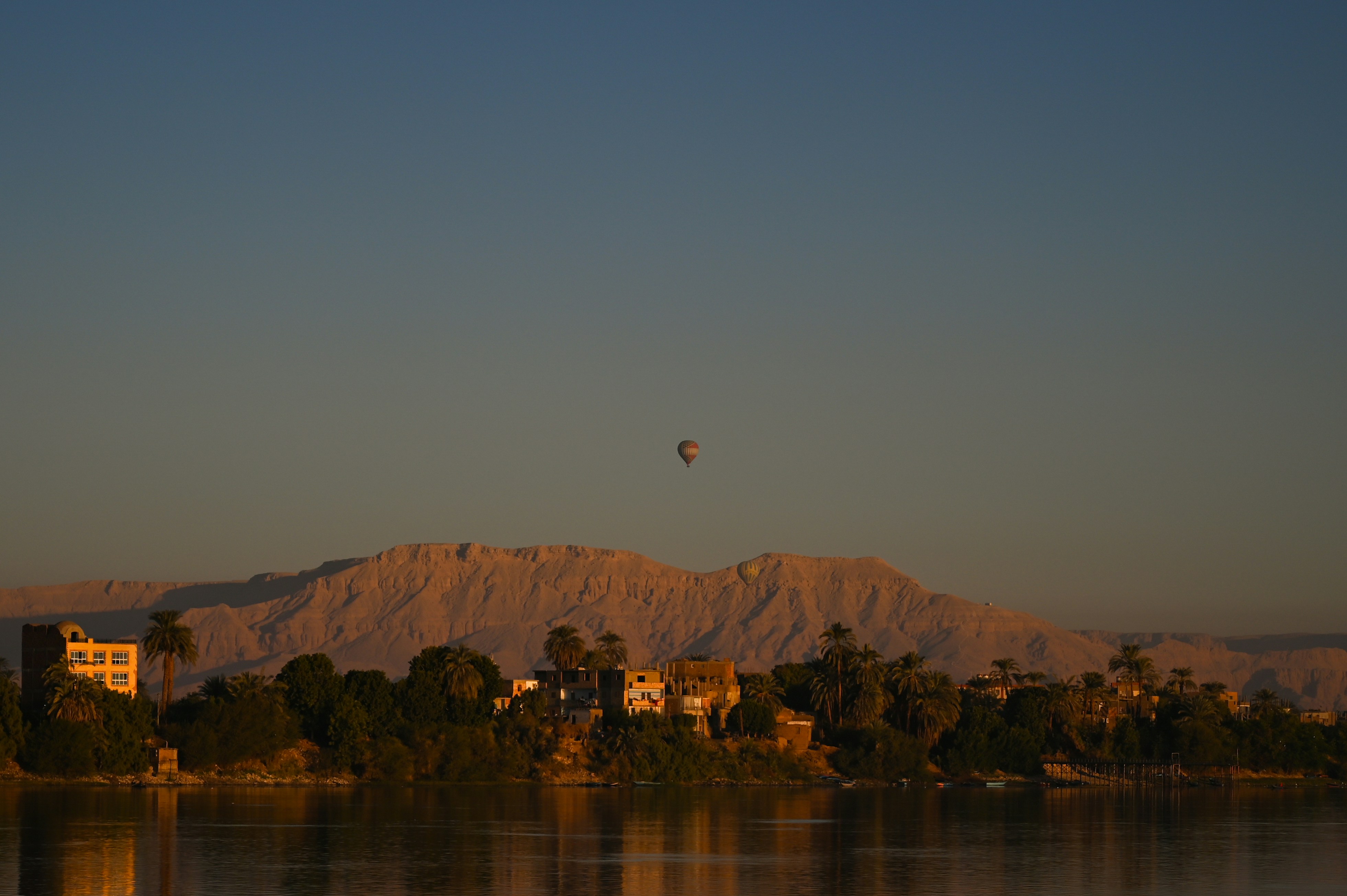 A balloon floats above a mountain range at dawn.