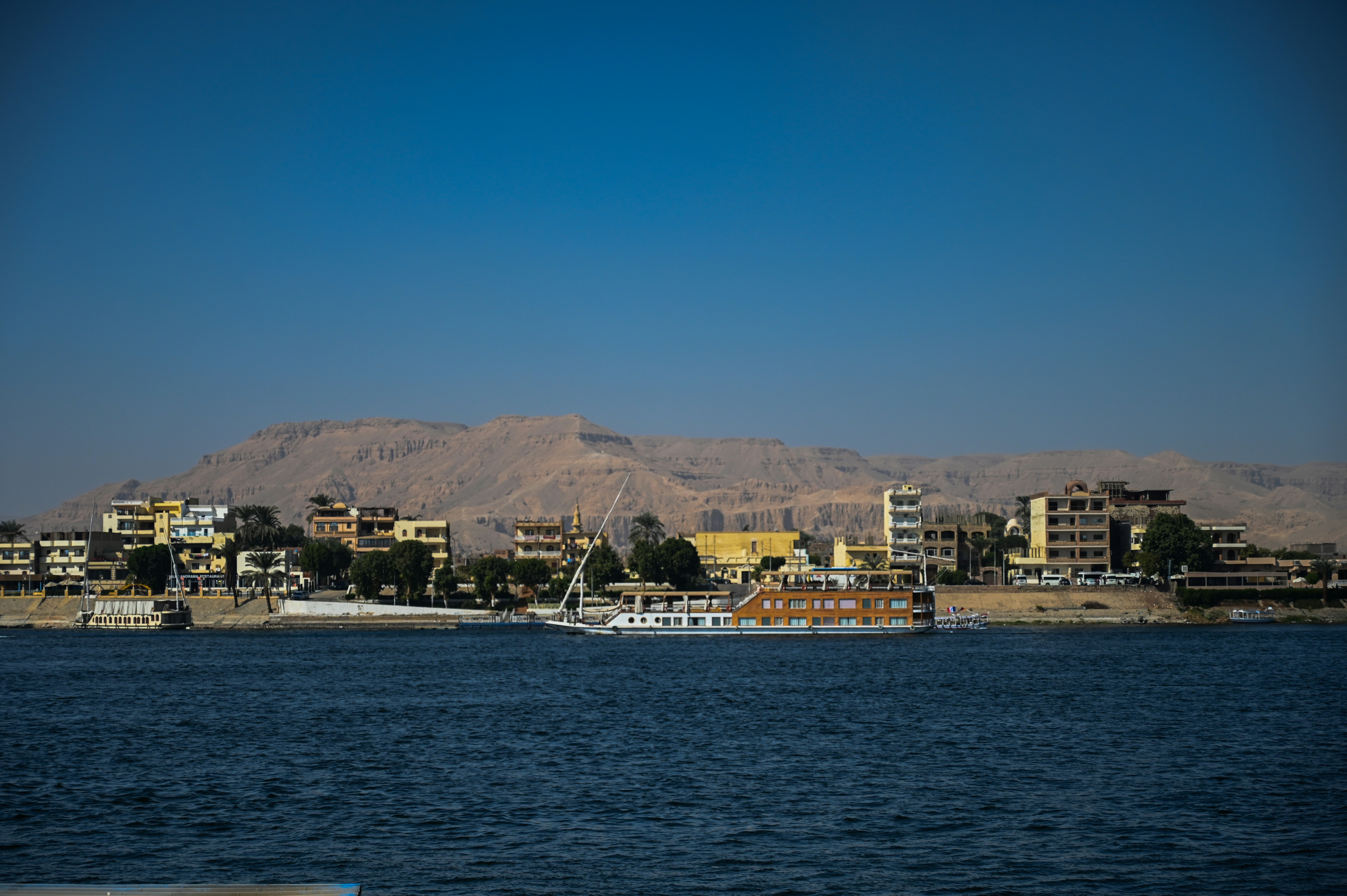 Water, buildings, and hills under a blue sky.