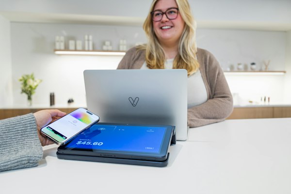 Dueña de un negocio sonriendo detrás de su laptop en el mostrador de su local, terreno de una agencia de marketing digital que se mide en clientes